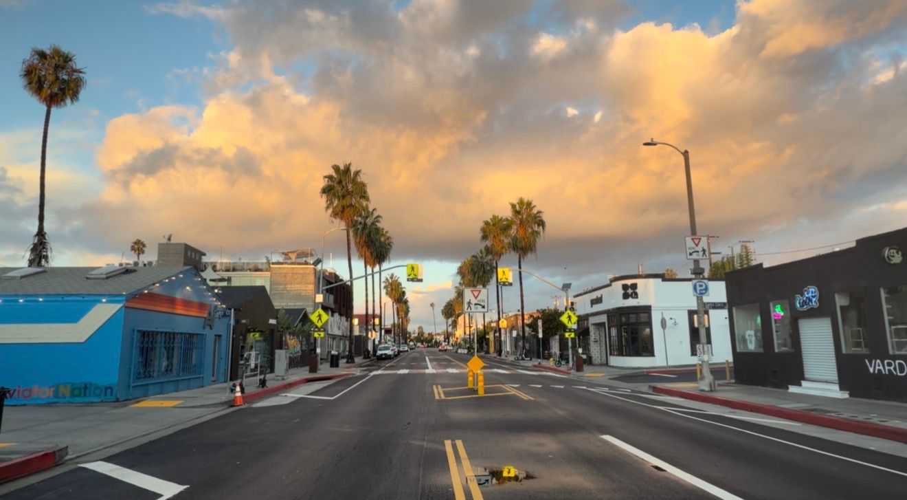 Panoramic view of a residential street with palm trees and colorful buildings under dramatic sunset clouds.