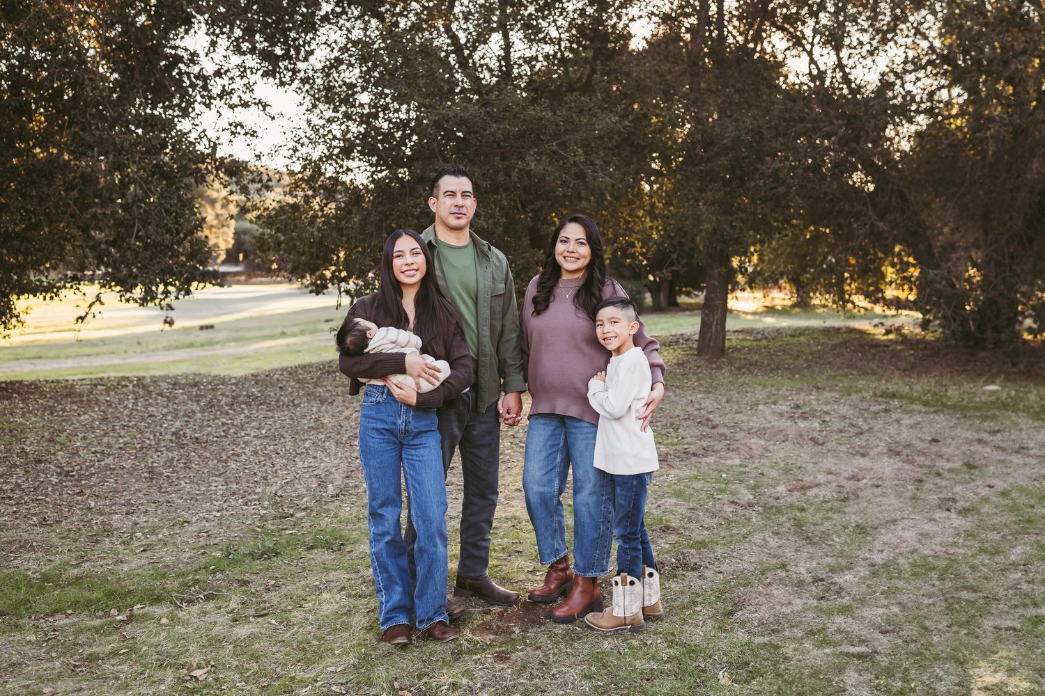 Family group poses together in casual attire during golden hour outdoor photo session at a rustic field location.