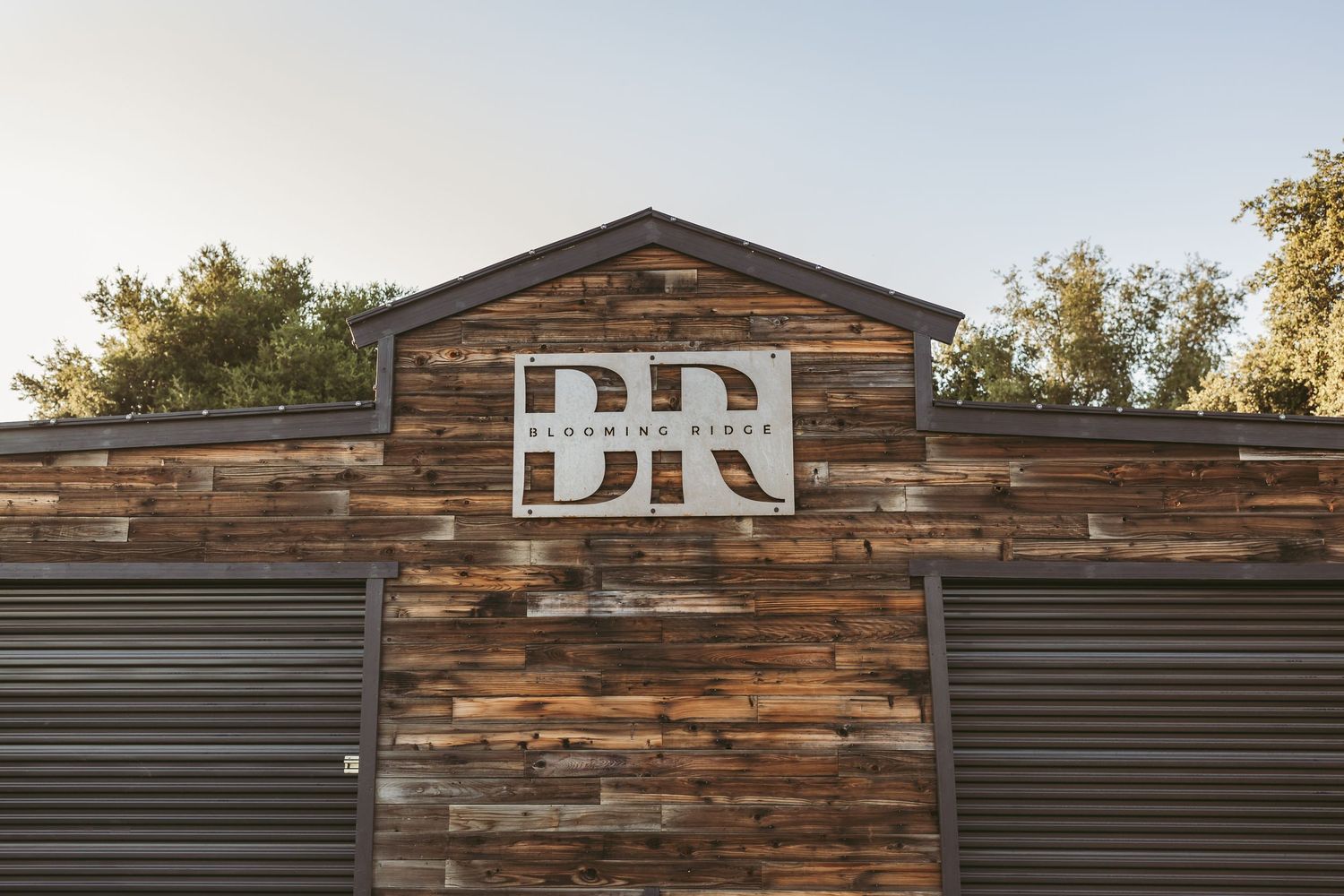 Rustic wood building exterior with white 'BR' letters mounted between two metal roll-up doors.