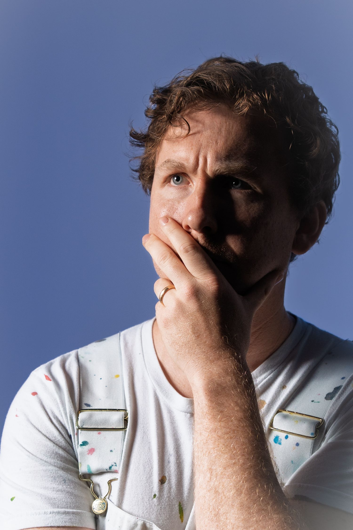 Someone expressing anxiety or distress covers their face against a blue-tinted background in a white shirt.