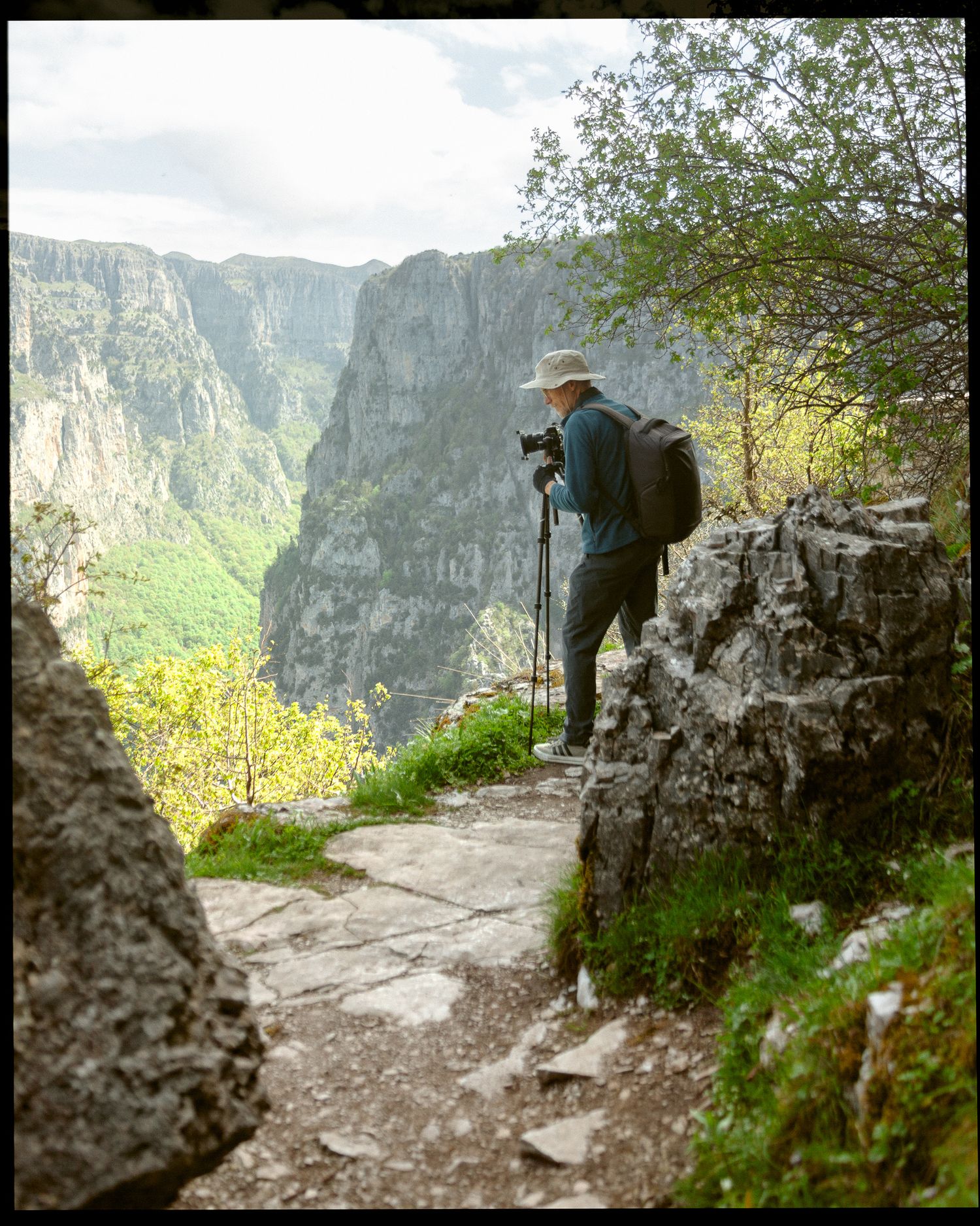 Photographer standing on rocky trail overlooking Vikos Gorge in spring light