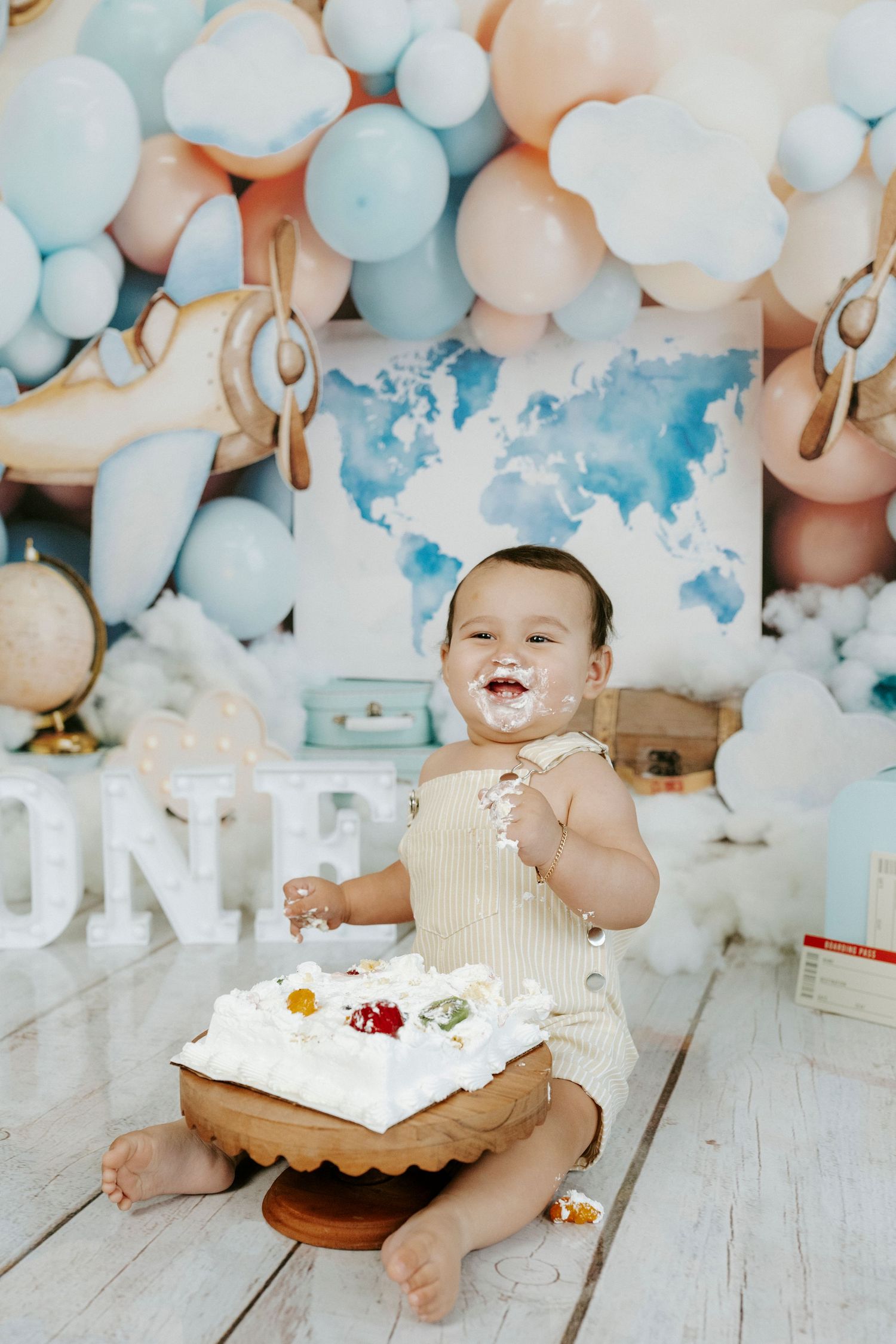Cake smash photo session featuring white and blue balloon decorations with a baby enjoying a white frosted birthday cake.