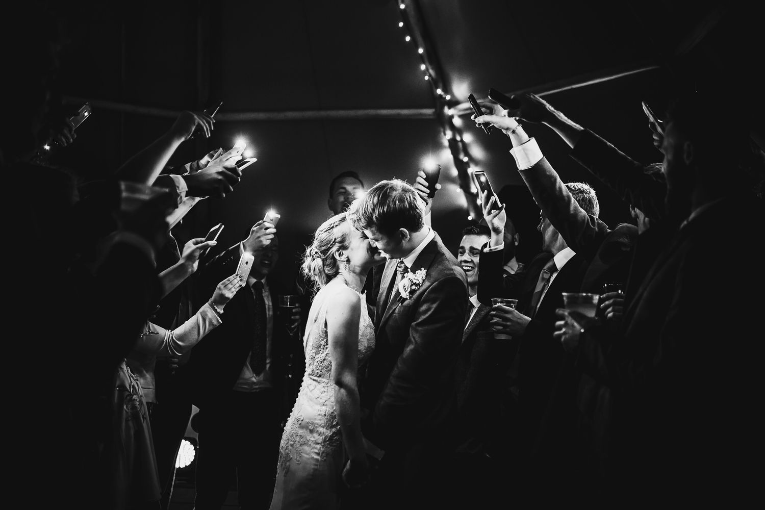 A black and white image of a couple at their wedding celebration surrounded by guests holding sparklers.