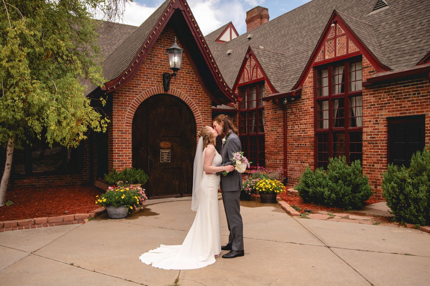 Two figures stand in an arched brick doorway surrounded by lush greenery at a historic church entrance.