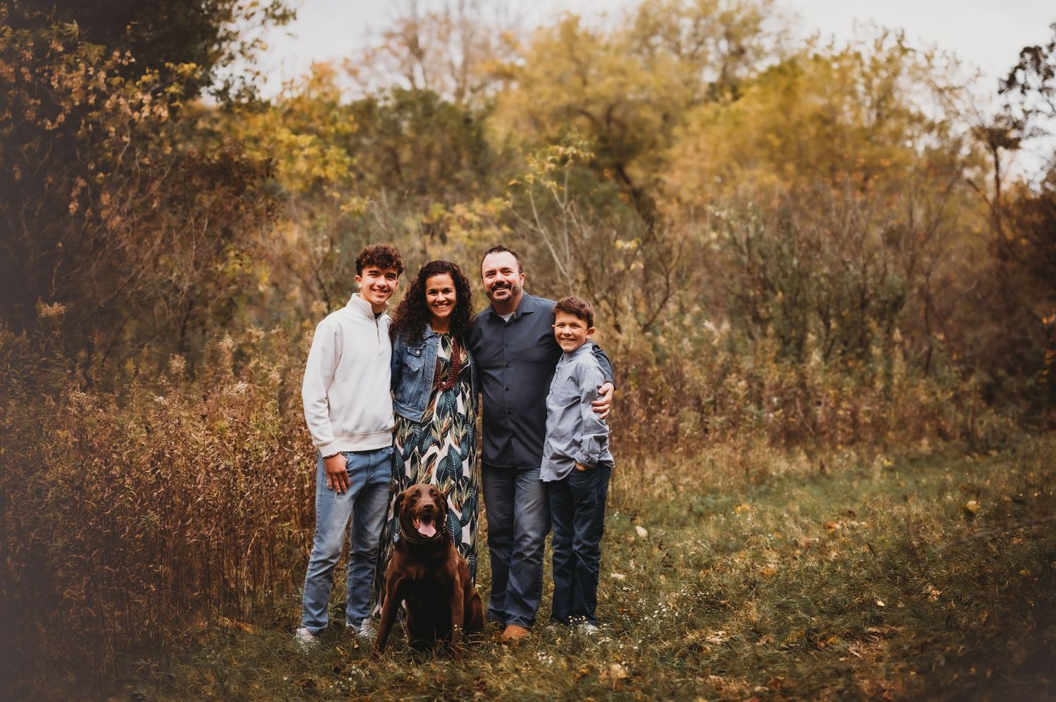 A small group stands together in an autumn field surrounded by golden foliage and trees.
