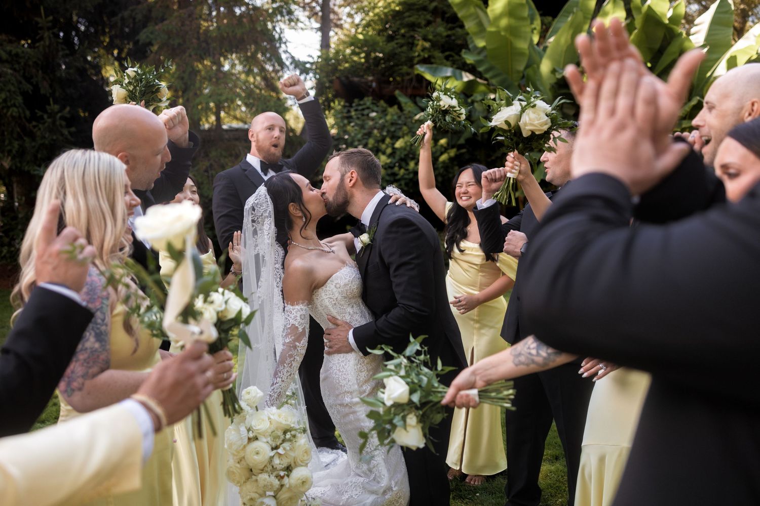 Wedding guests stand in rows outdoors clapping and celebrating during a joyful ceremony.