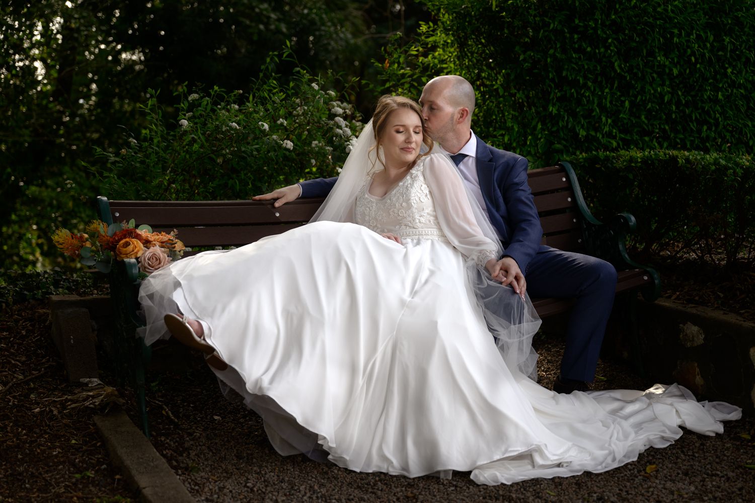 A romantic wedding couple poses in a garden setting during their outdoor photo session.