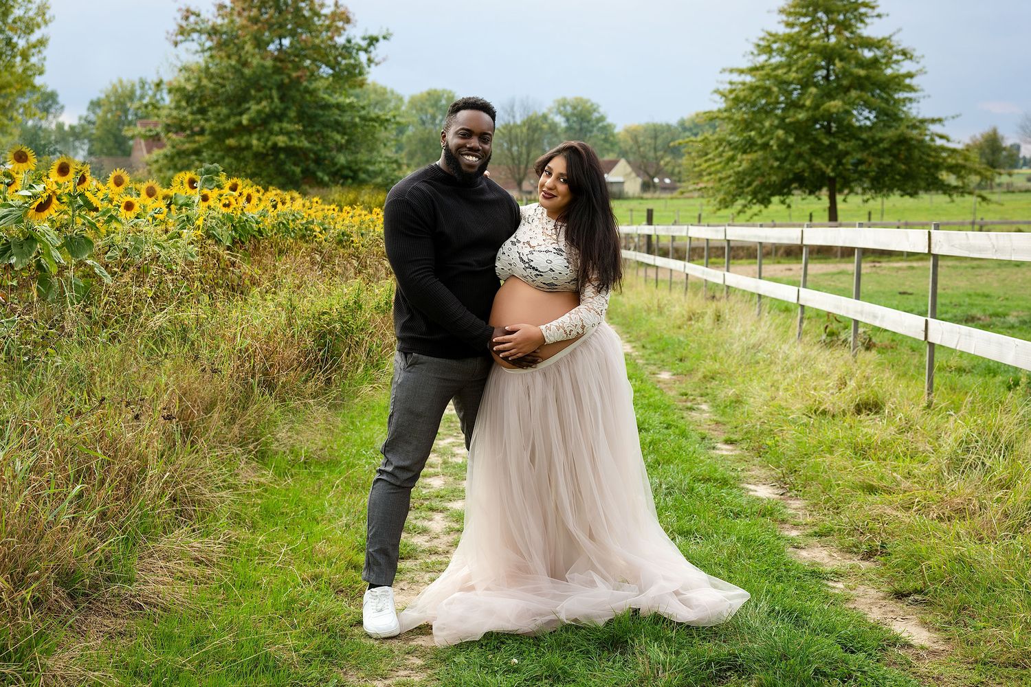 Pregnant woman in pink dress poses gracefully in maternity photoshoot against white background.