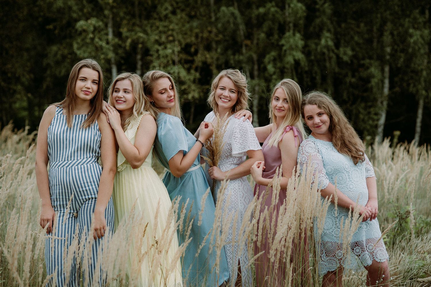 A group in coordinated blue and yellow dresses pose together in a rustic outdoor setting.