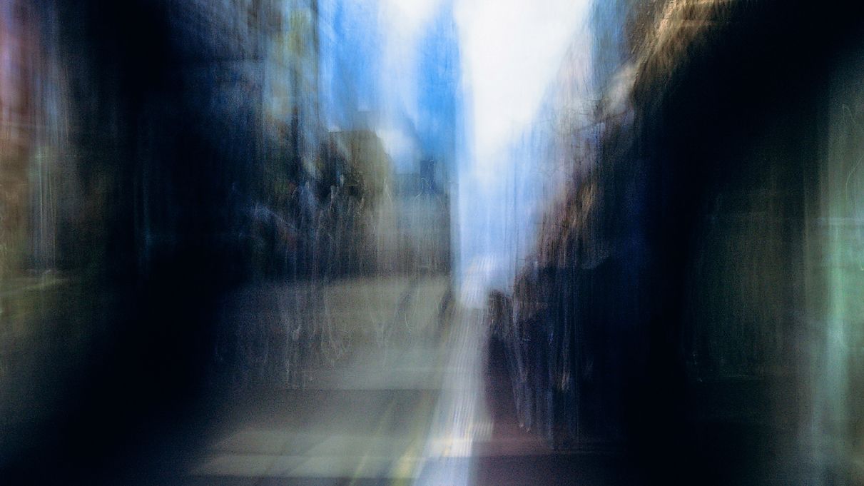 Blurred motion effect of people walking through a modern urban corridor with glass walls and natural lighting.