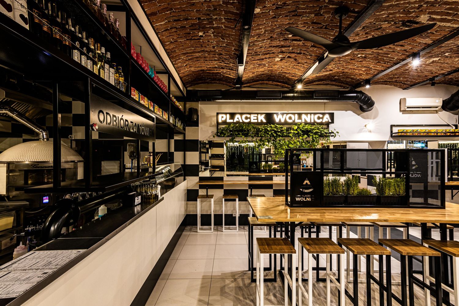 Wnętrze restauracji Placek Wolnica z ceglanym sklepionym sufitem, barem oraz drewnianymi wysokimi stołami.