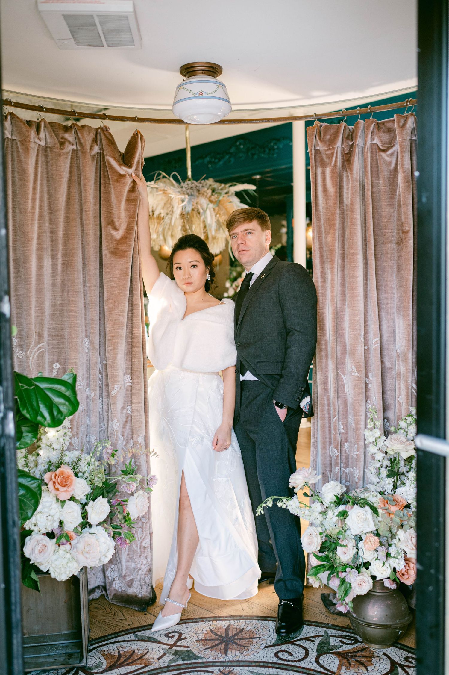 Couple posing in front of floral-decorated curtains with romantic lighting.