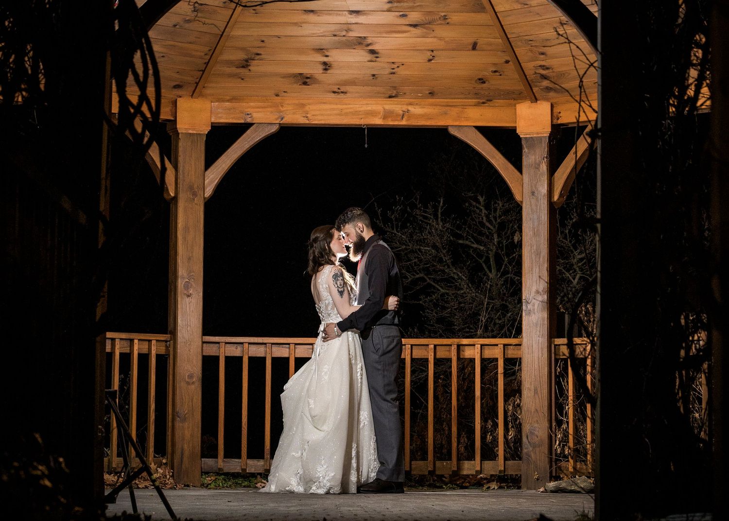 Newlyweds share an intimate moment outdoors with autumn foliage and rustic architecture in background.