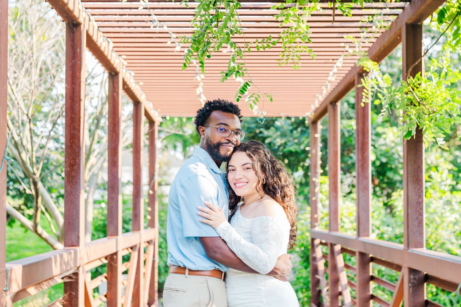 Couple shares romantic moment at sunset in outdoor wooden deck surrounded by lush greenery.