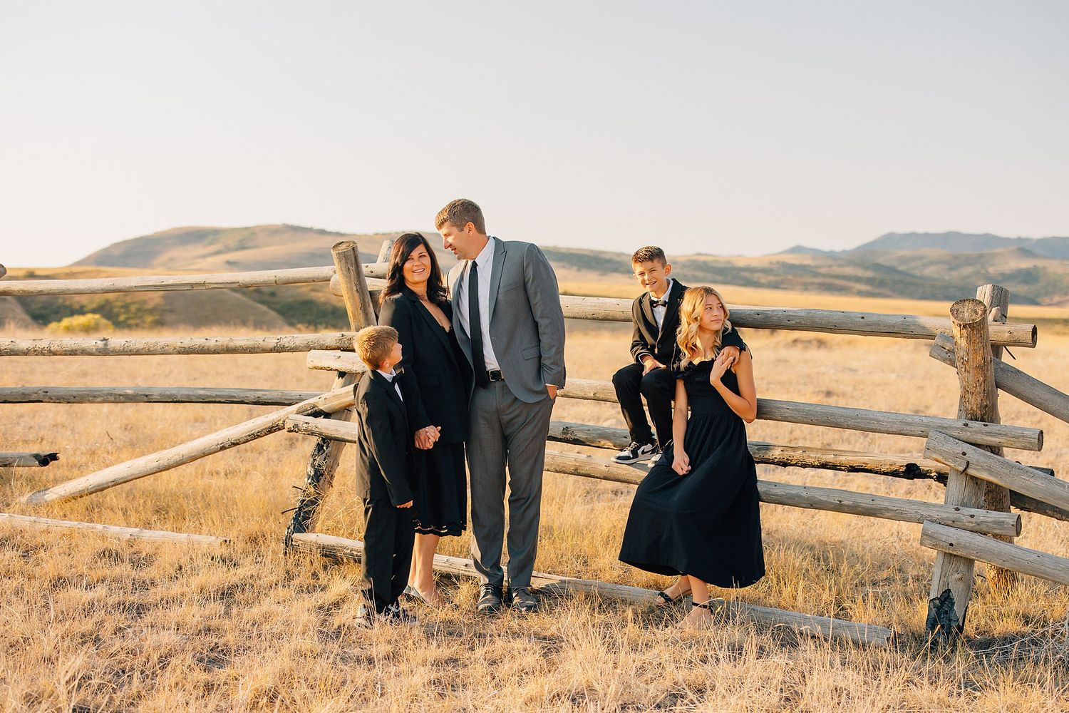 A group of people in black and navy outfits stand together in a golden field at sunset.