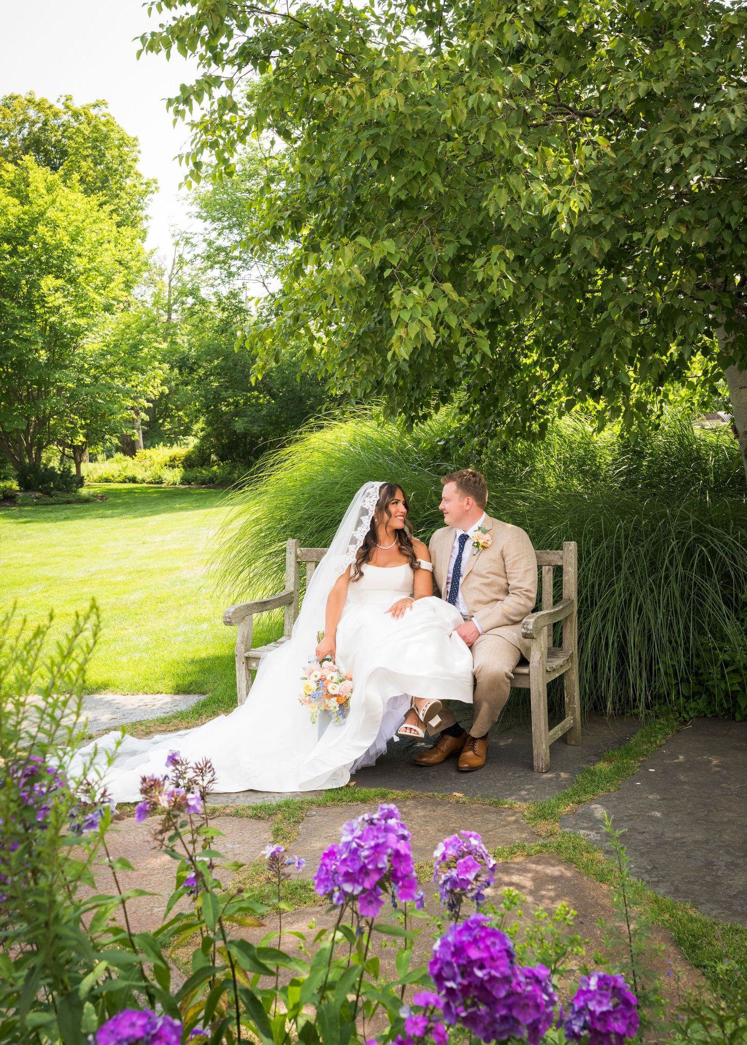 Bride and groom share a romantic kiss outdoors, bride holding colorful bouquet in white gown with veil on wedding day.