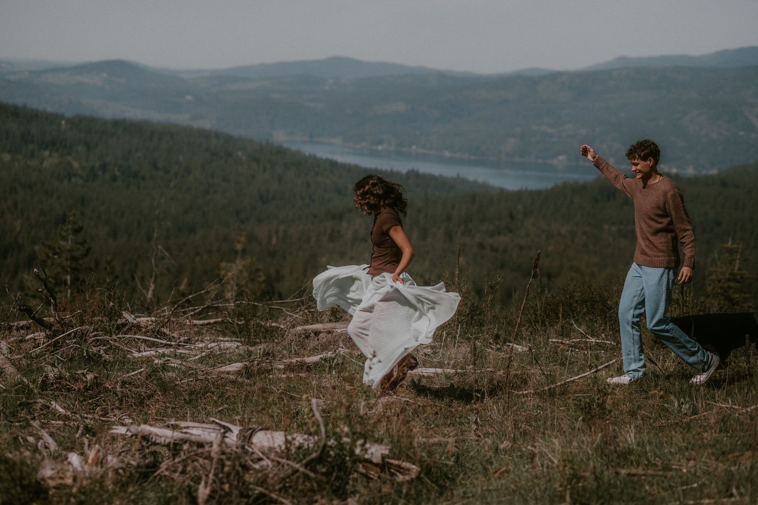 Couple dancing on a mountain hilltop surrounded by lush forest and lake views, bride in flowing white dress.