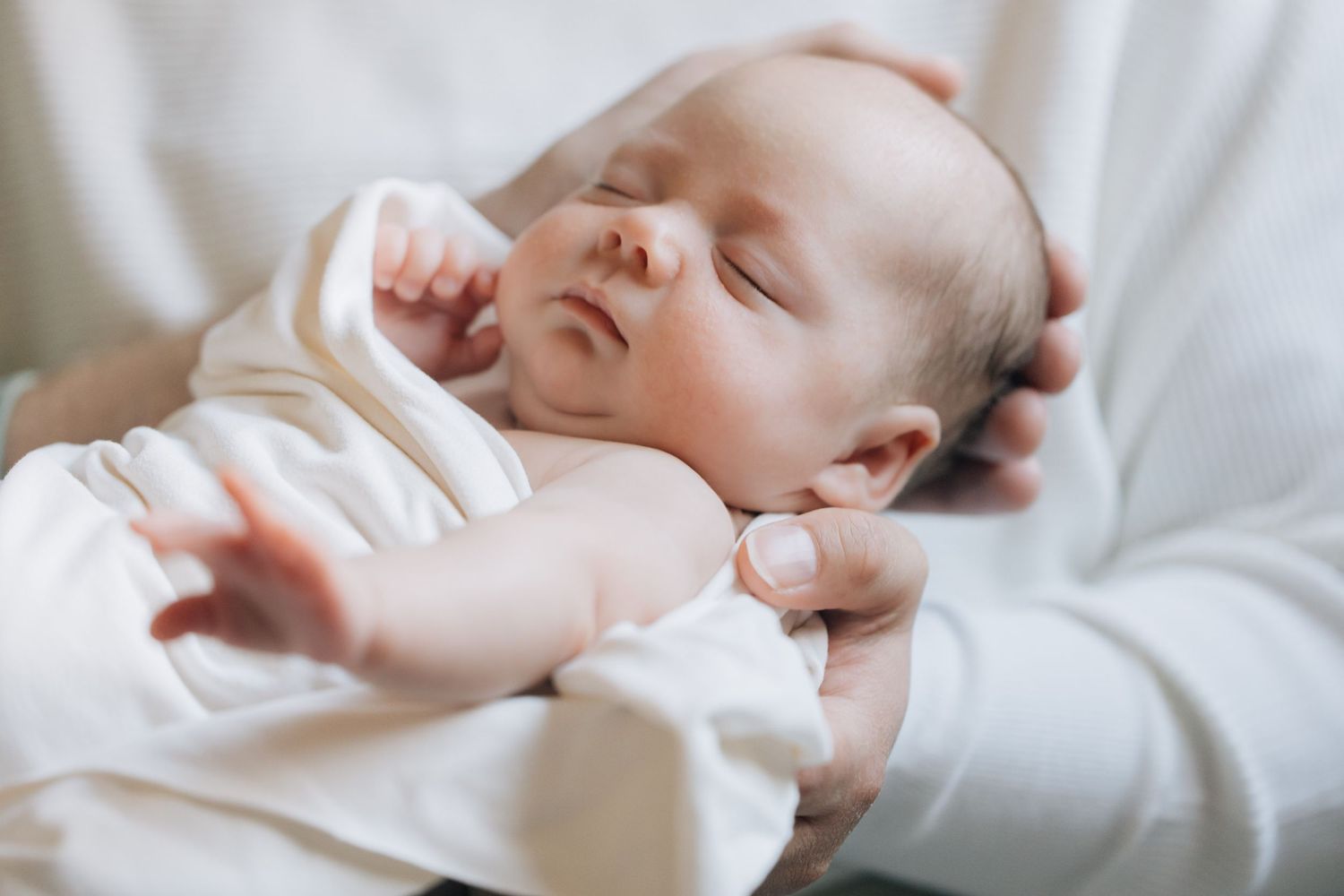 Sleeping newborn baby resting peacefully in parent's gentle hands.