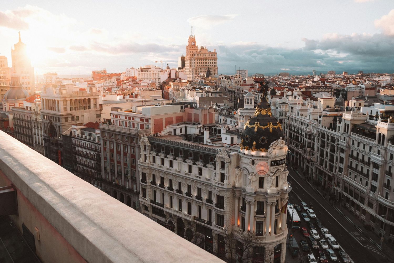 Panoramic cityscape view of Madrid's historic Gran Via street with ornate buildings and dramatic sunset sky.