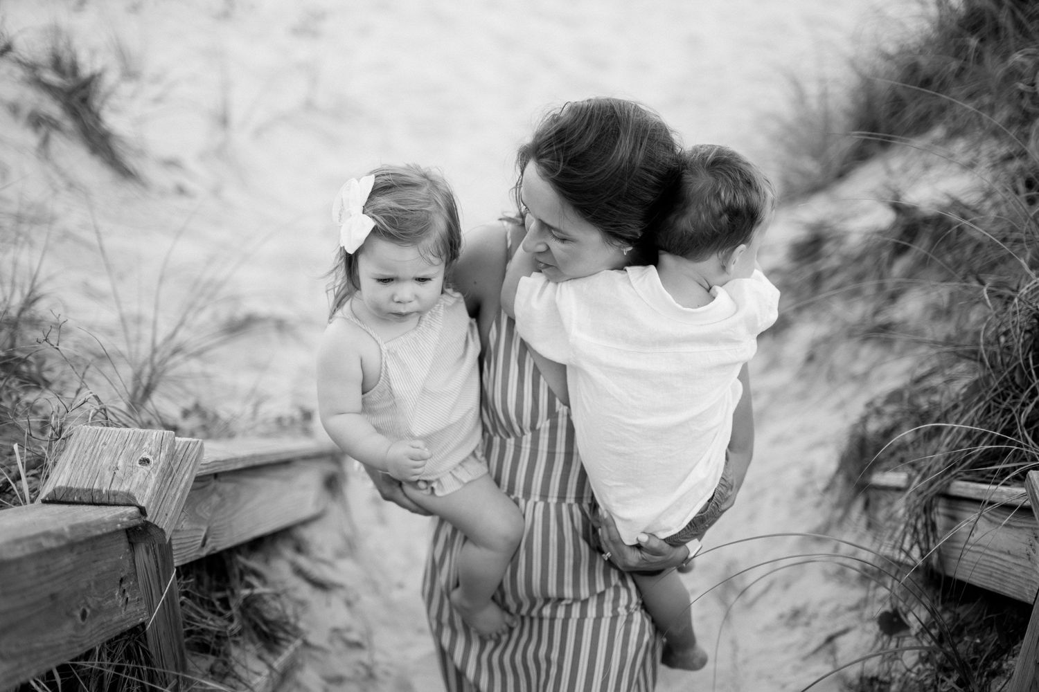 Black and white photo of a mother holding two young children on sandy beach steps among dunes.