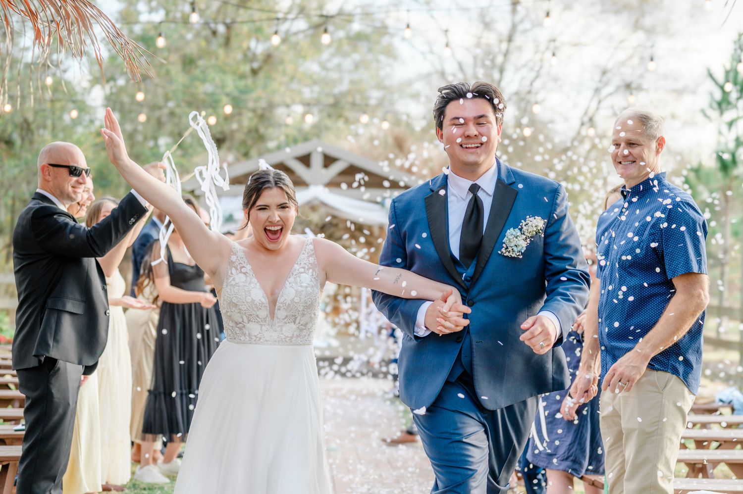 Wedding party celebrates with confetti toss in outdoor garden setting wearing navy blue and white attire.