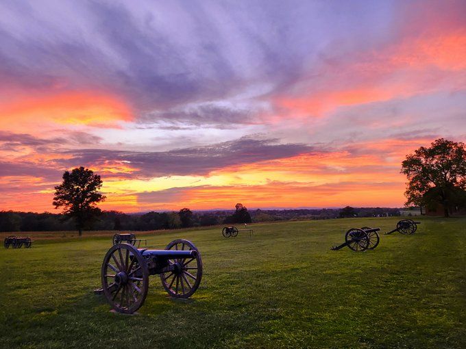 Dramatic sunset over battlefield with Civil War cannons silhouetted against colorful sky.