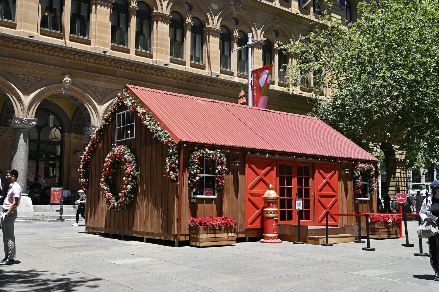 Festive Christmas cabin display with red roof and wreaths outside a historic building.
