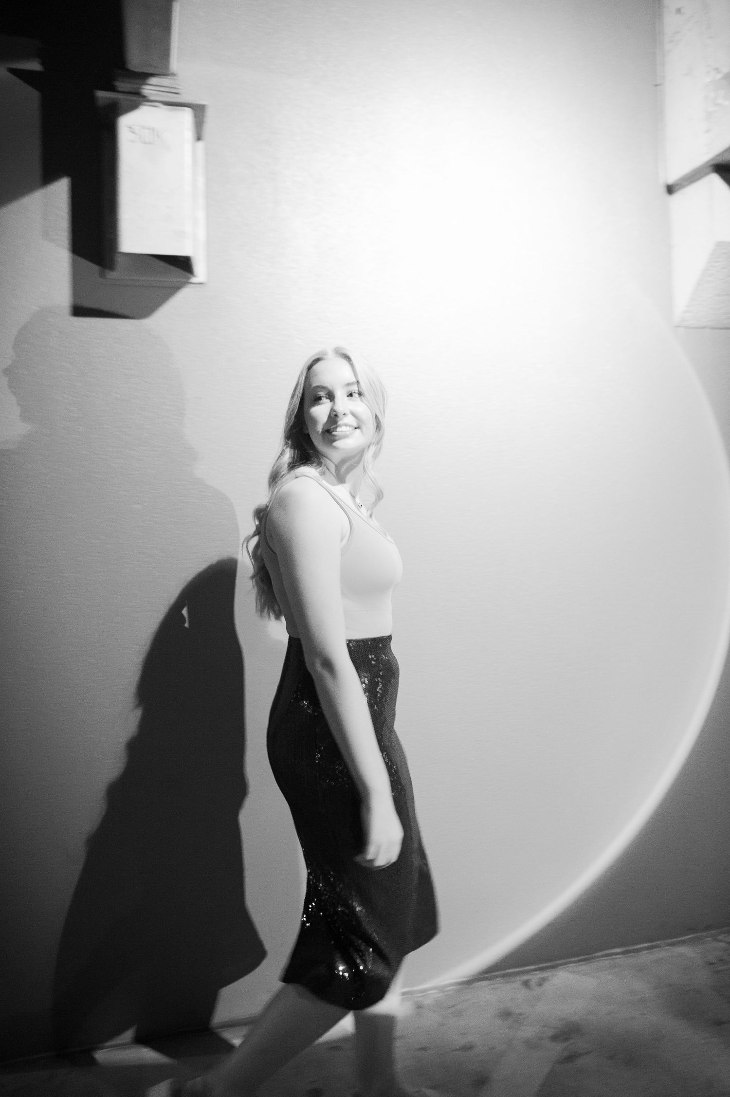 A black and white photo series showing a figure in a dark dress posing against a white wall with dramatic shadows.