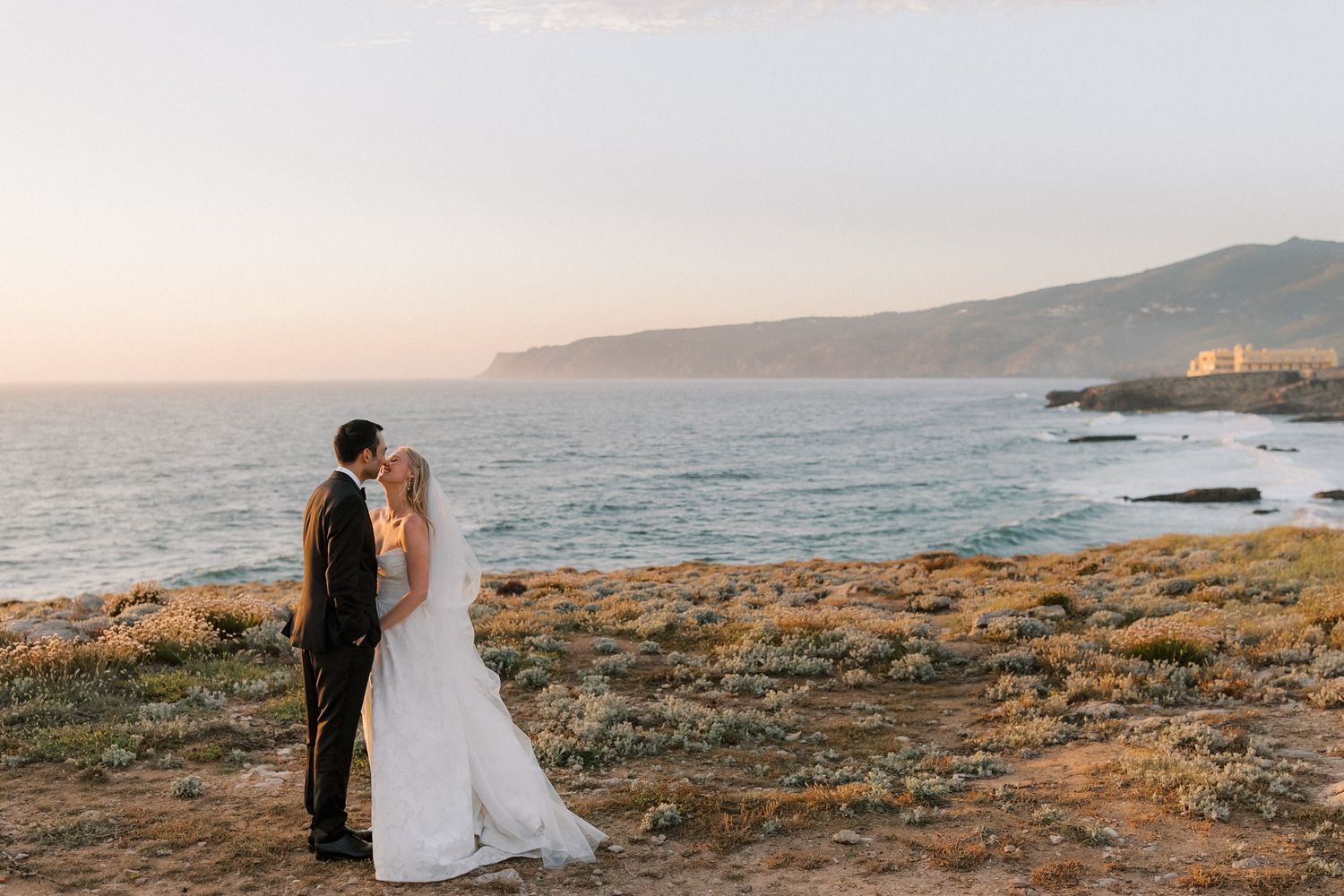 Bride and groom sharing a sunset kiss overlooking the Atlantic Ocean during their destination wedding at Arriba by the Sea in Cascais, Portu