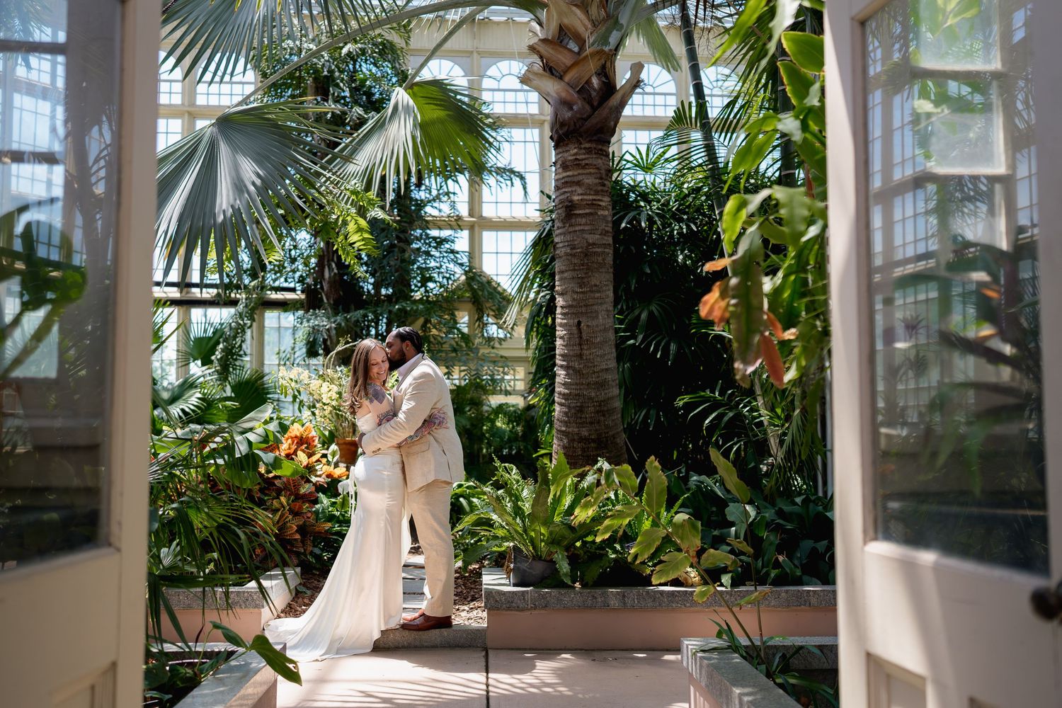 Bride and Groom sharing a romantic kiss in a lush tropical greenhouse conservatory during their wedding ceremony, in Baltimore, MD