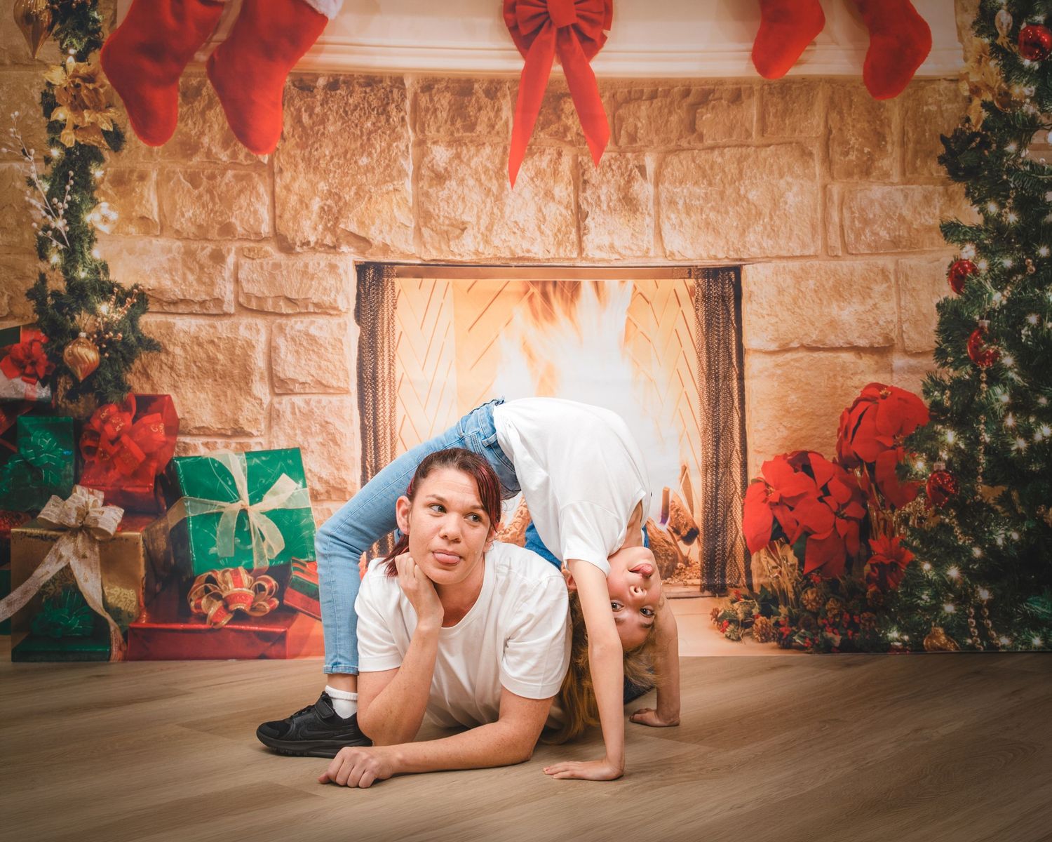 Awkward family photo of mum and daughter wearing matching clothes, mum lying under girl doing backbend, in front of a christmas fireplace
