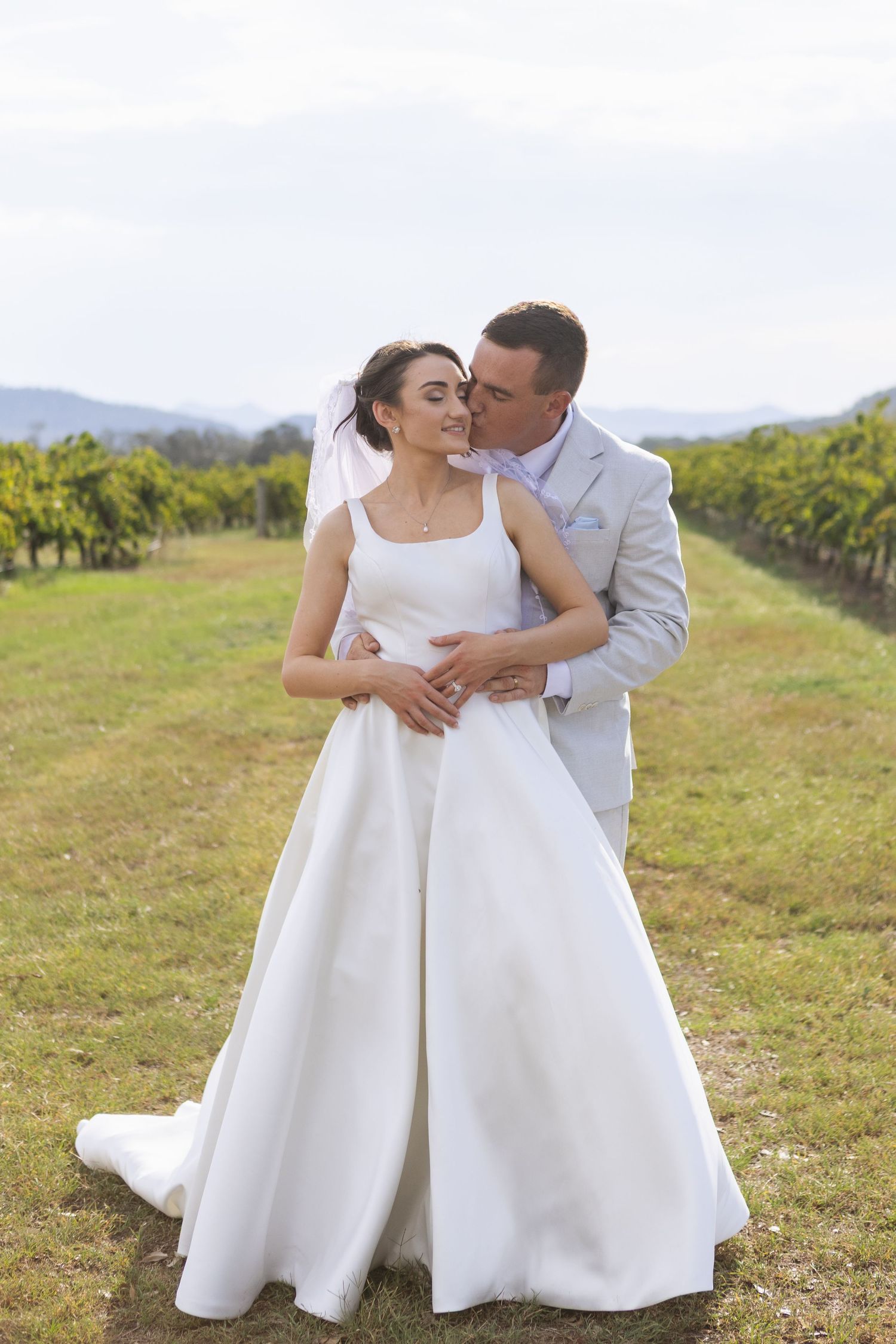 Groom hugging bride from behind and kissing at two rivers winery on their wedding day