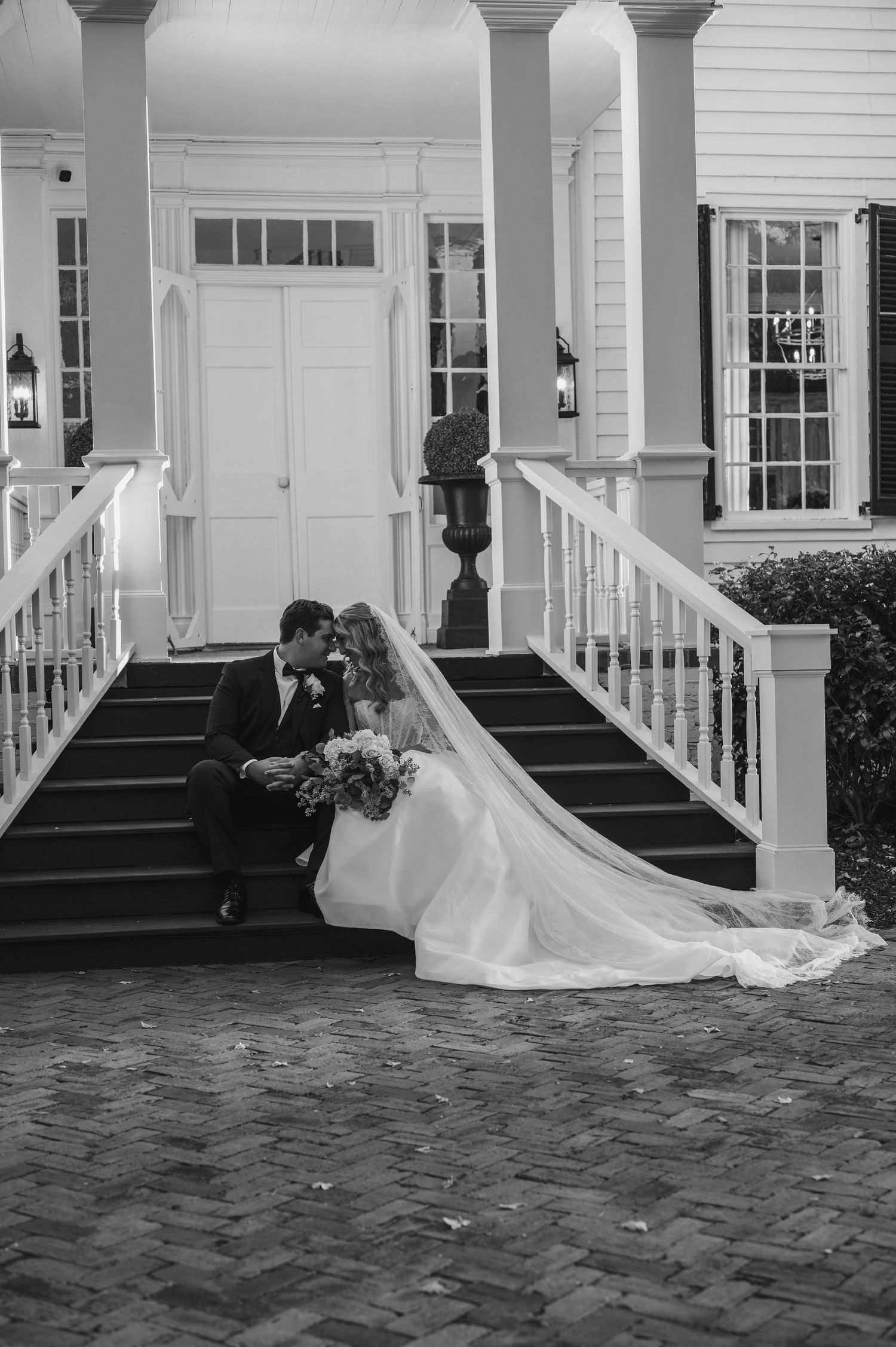 A romantic black and white photo series showing a bride and groom in elegant poses on a porch of a classic home.