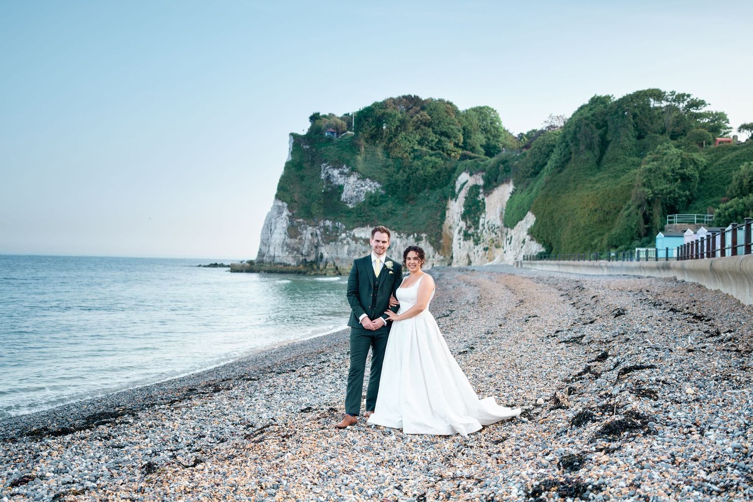 Bride and groom posing on a pebble beach with St Margaret's white chalk cliffs and lush greenery in the background.