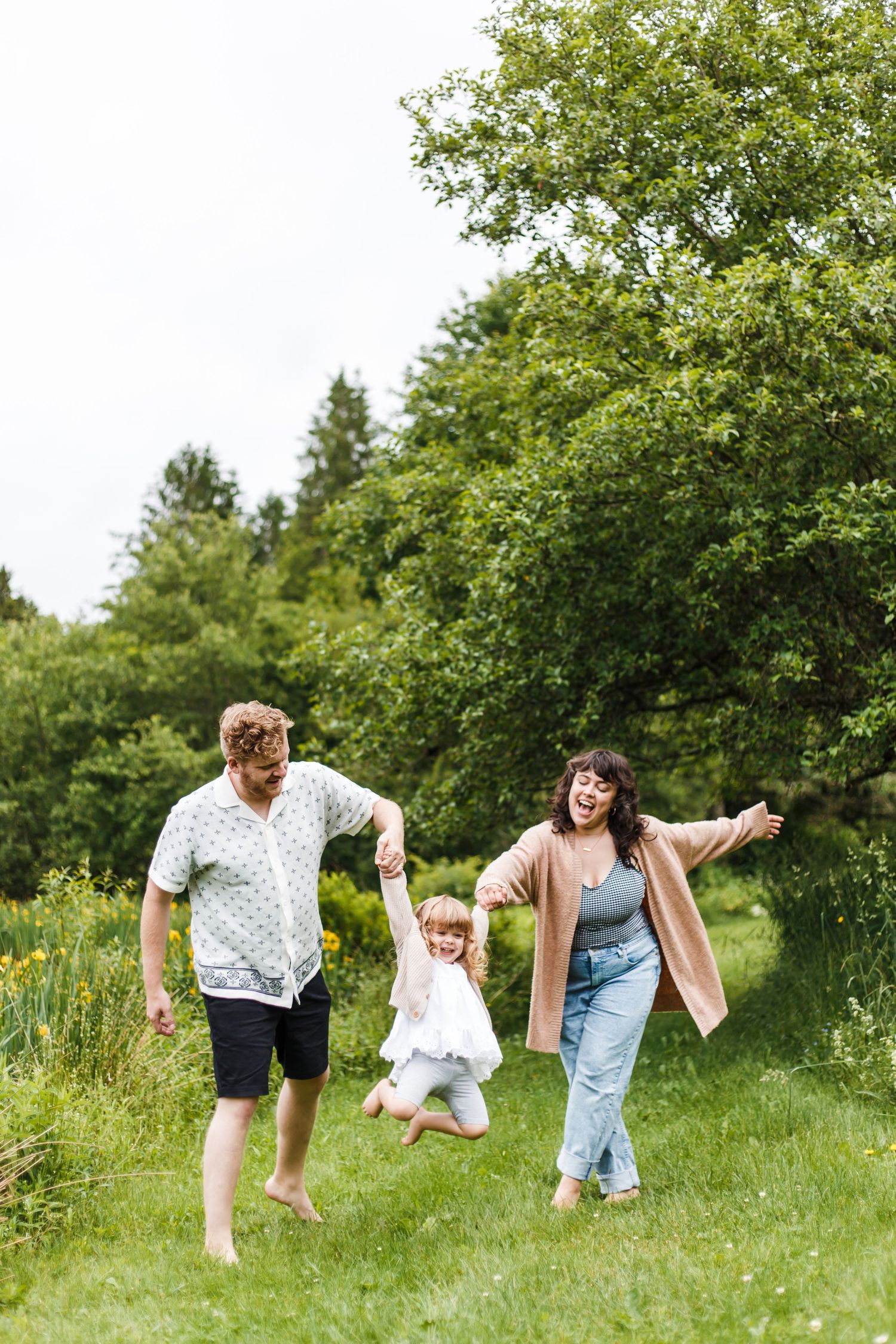 Family sitting on a wooden dock by a pond surrounded by lush greenery and yellow flowers on a summer day.
