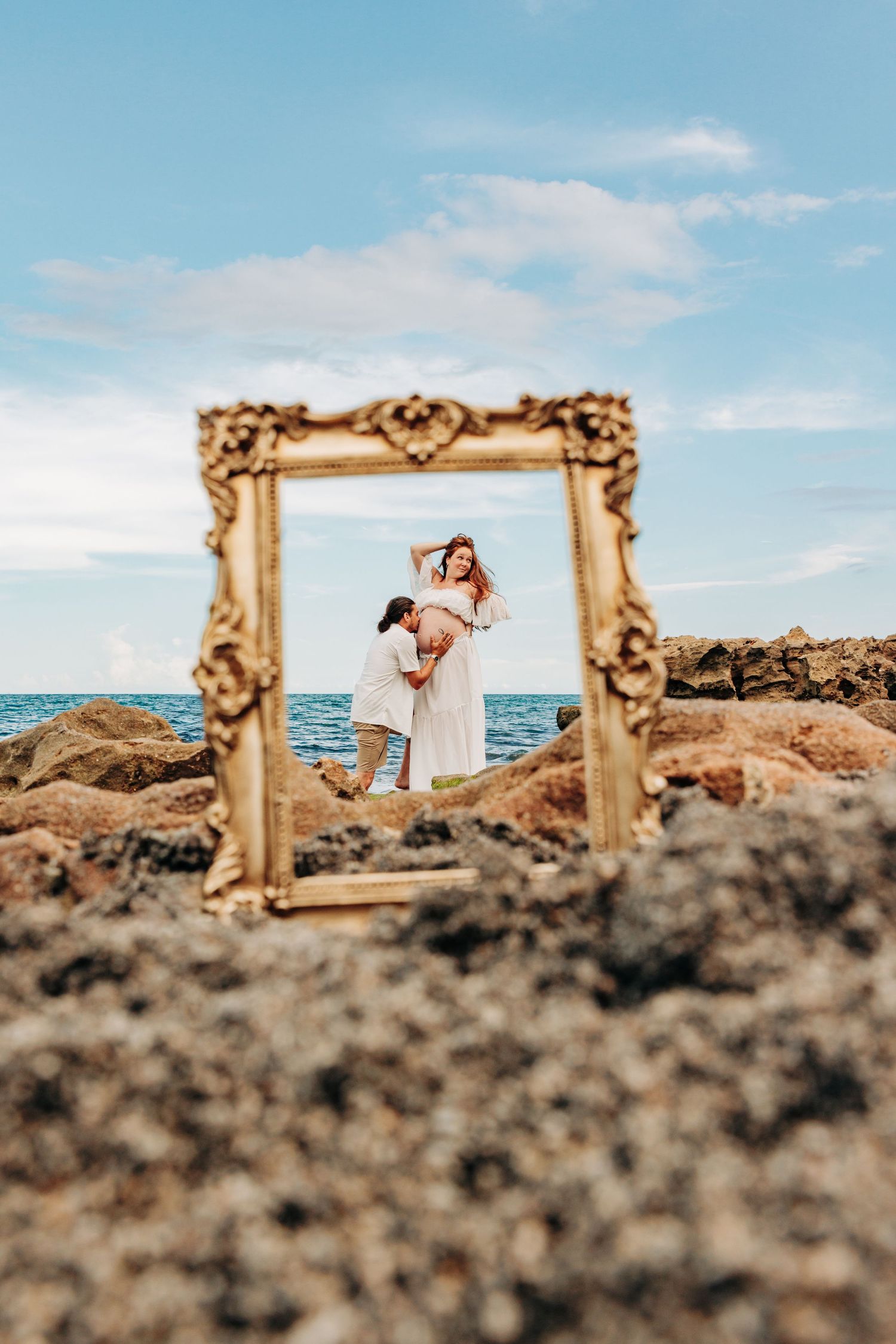 Maternity photographer Jupiter FL portrait of an expecting couple framed against the rocky shoreline and ocean at Coral Cove Beach.