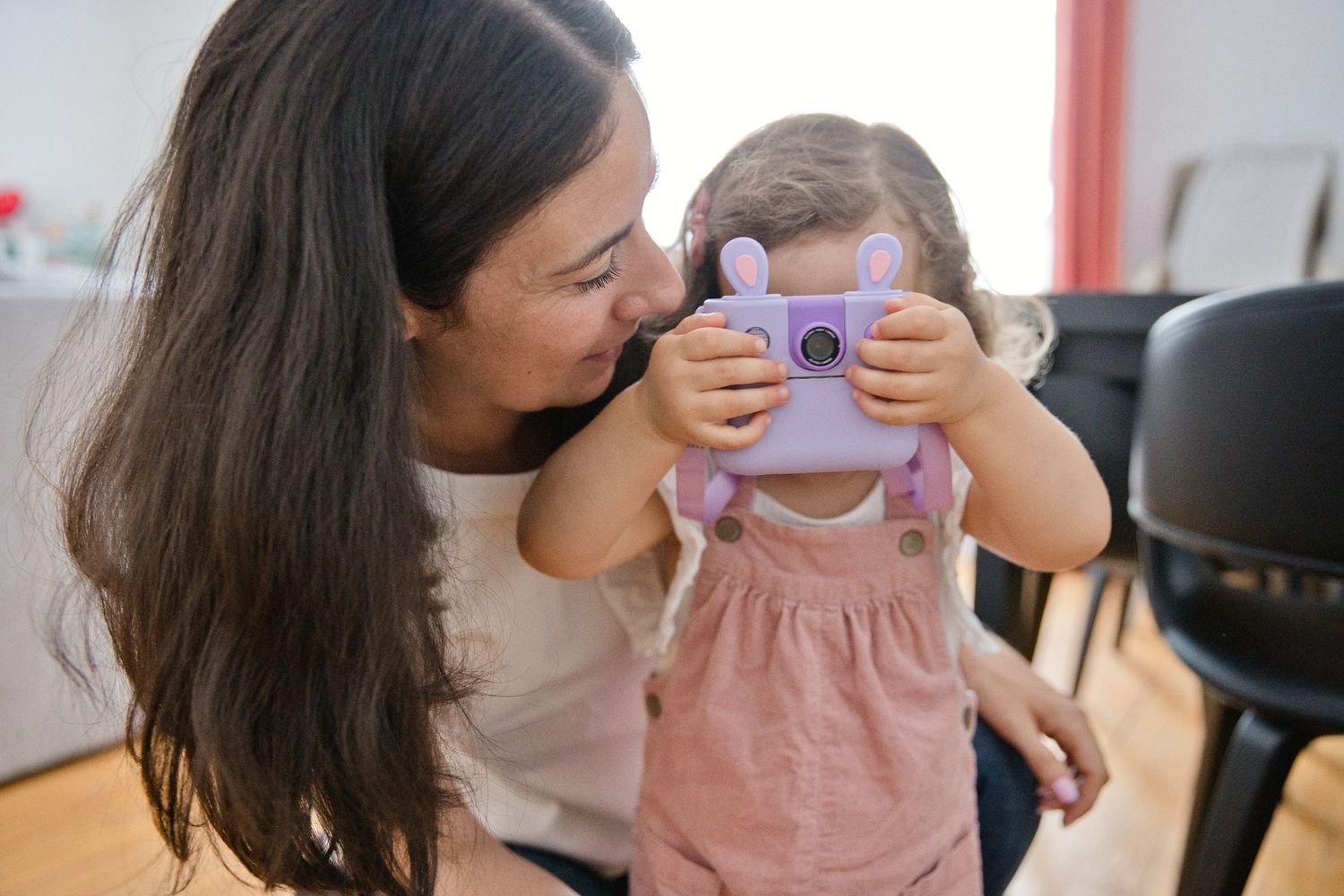 Une petite fille timide se cache derrière son appareil et prend en photo la photographe pendant un shooting en famille naturel à Asnières