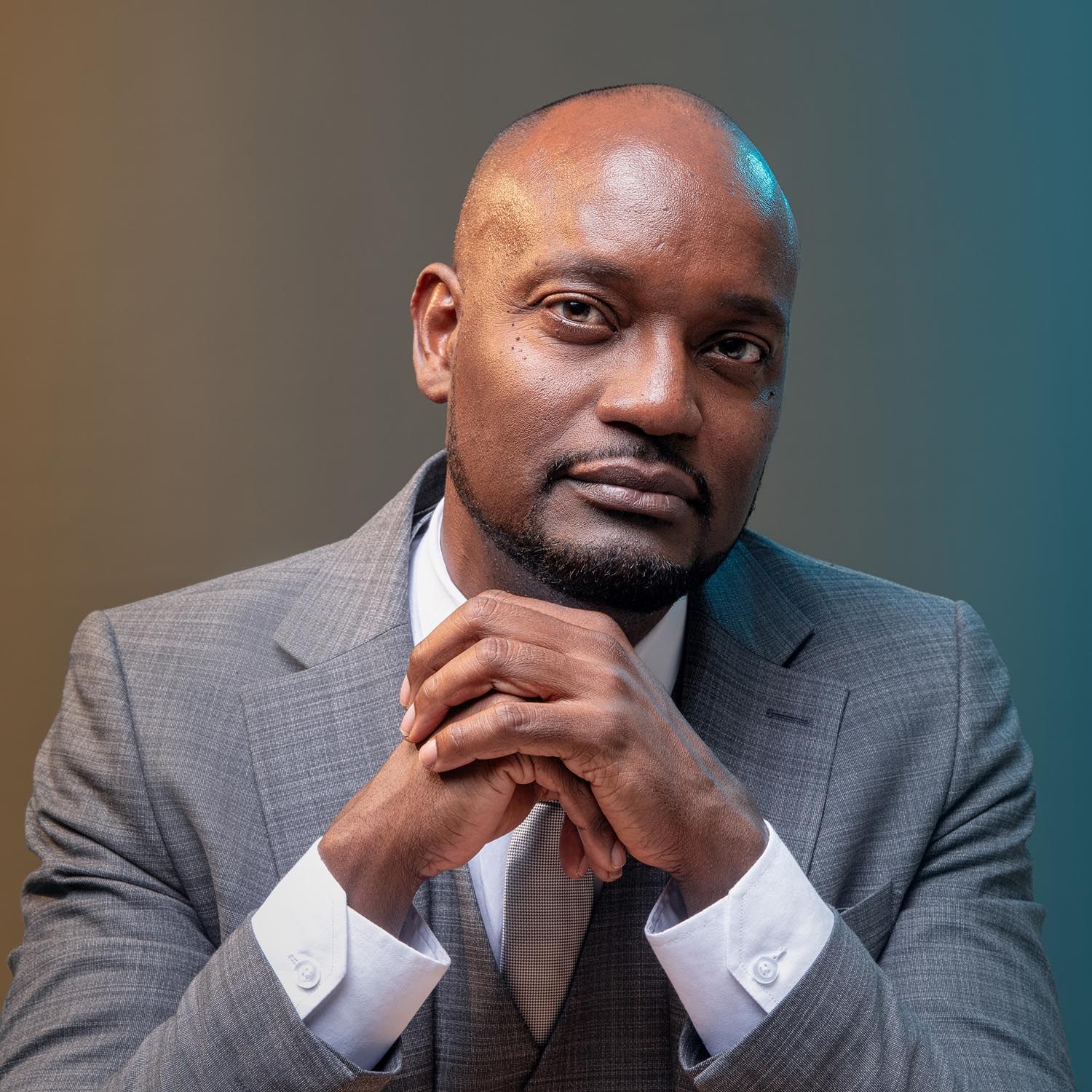 Dennis Martis, diputado of Bonaire, sitting for a portrait in a grey suit with his hands  in Kralendijk in Felicia Schuette's photo studio.
