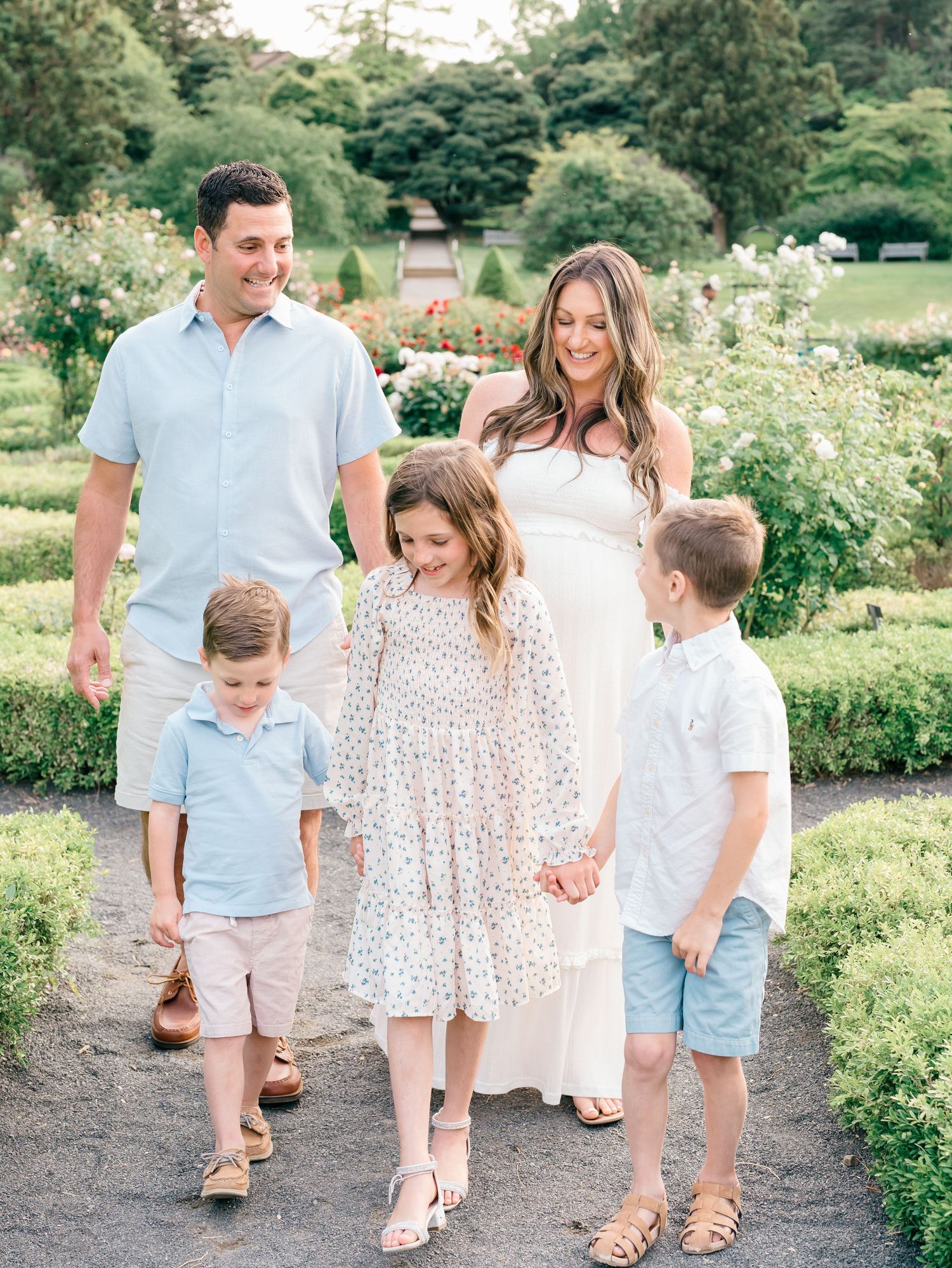 Family walking hand in hand along a garden path at Deep Cut Gardens in Monmouth County, NJ, with the mother expecting.