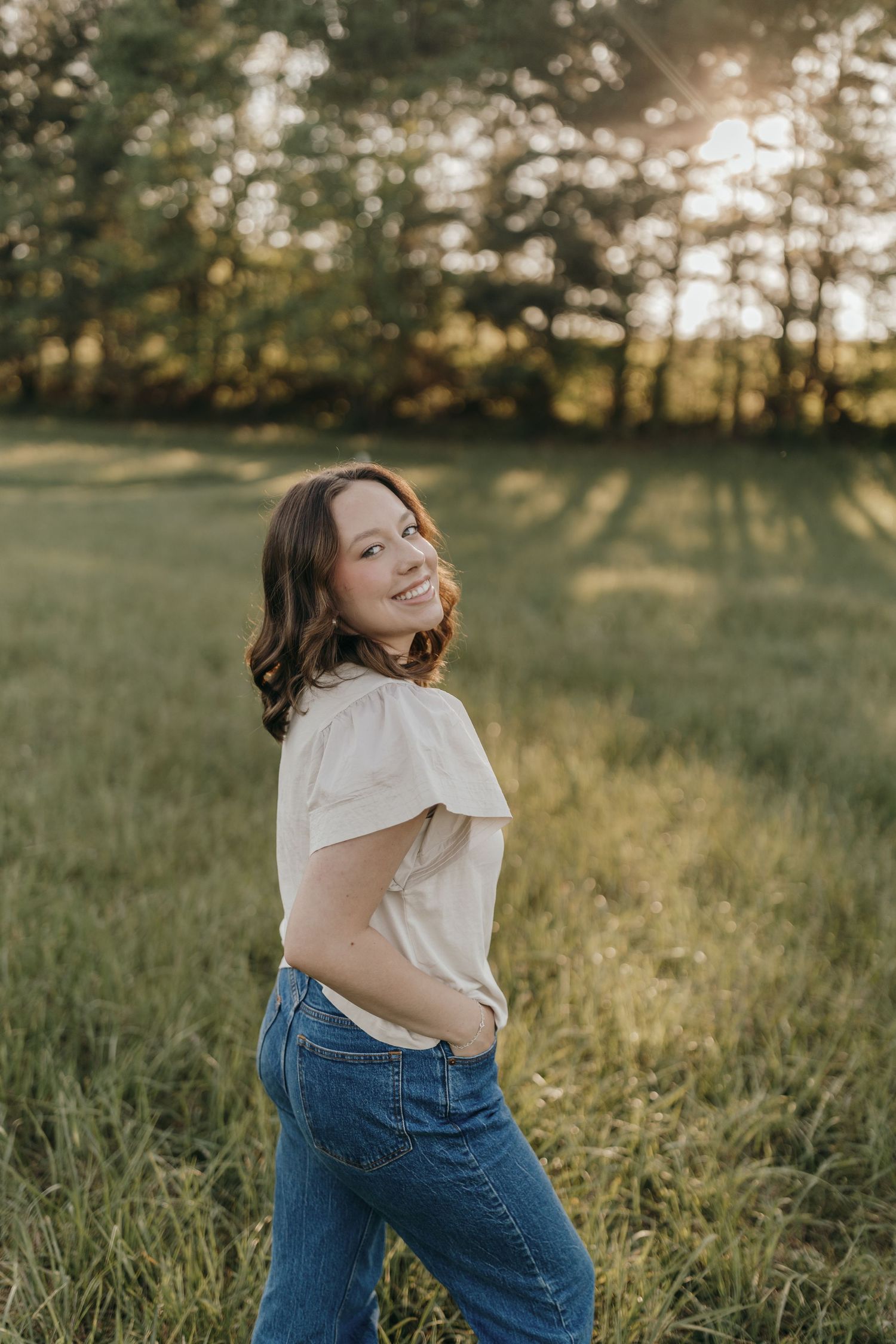 Portrait in golden hour lighting with person in white top and jeans in grassy field.