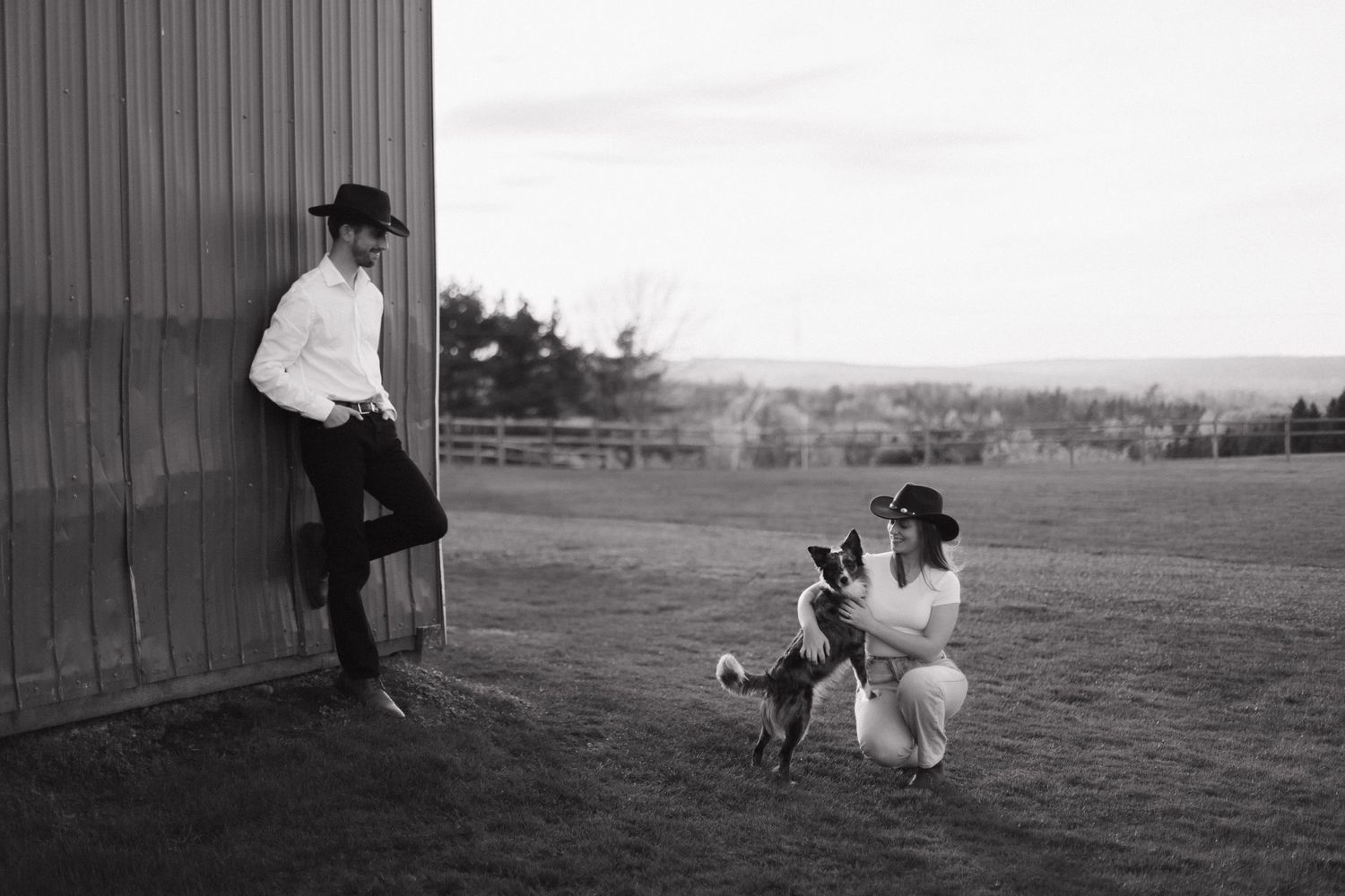 Black and white vintage photo of two people and a playful goat in a rural farmland setting.