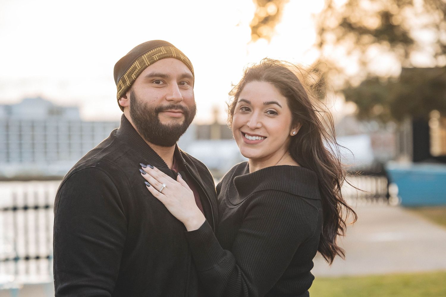 A couple poses for an engagement photo at sunset near a waterfront.