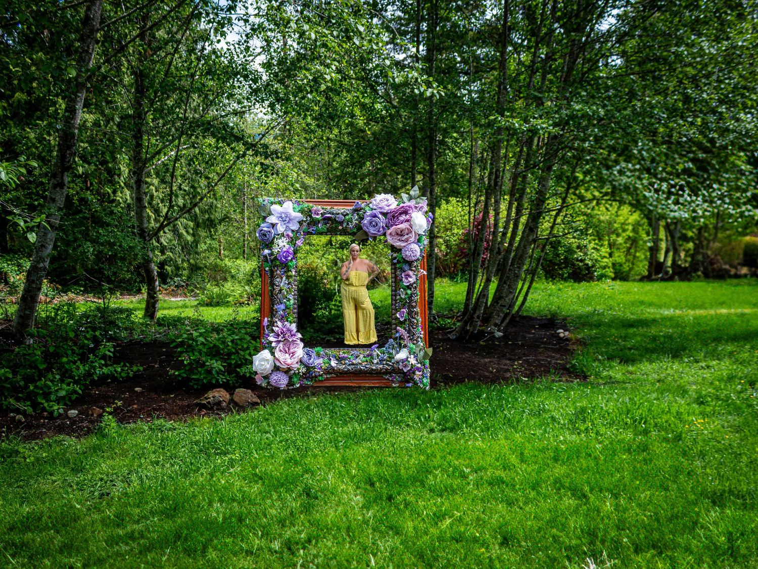 A floral archway decorated with purple and pink flowers stands in a lush green garden setting.