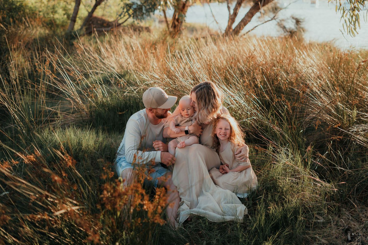 A family shares an intimate moment in tall golden grass at sunset.