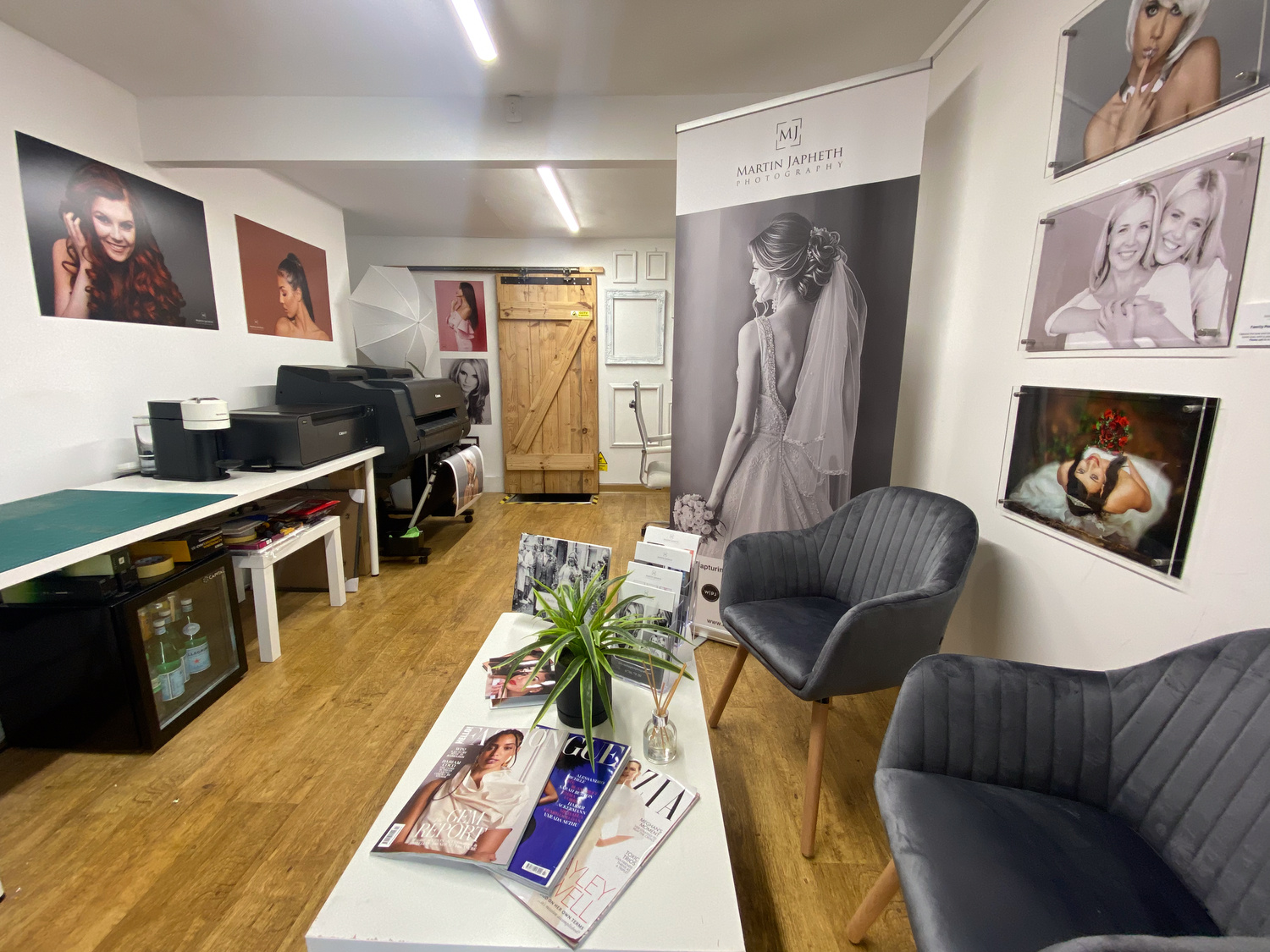 Photography studio interior with framed portraits, comfortable seating, and hardwood floors.