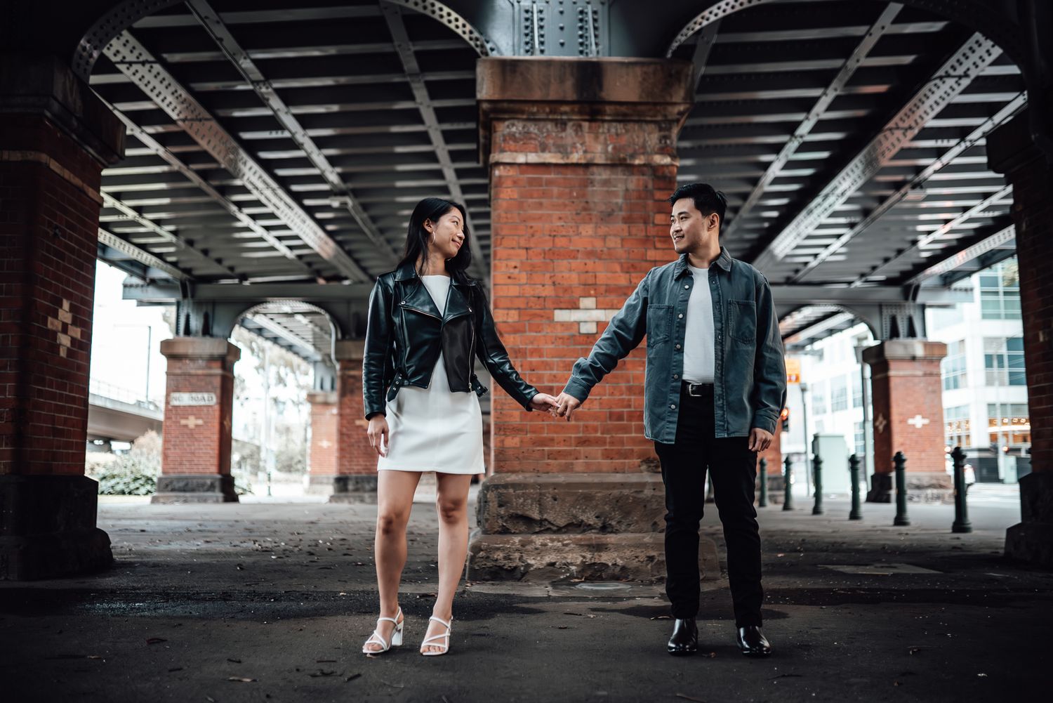 Couple holding hands under urban bridge architecture in modern city setting taken by Melbourne casual couples and engagement photographer