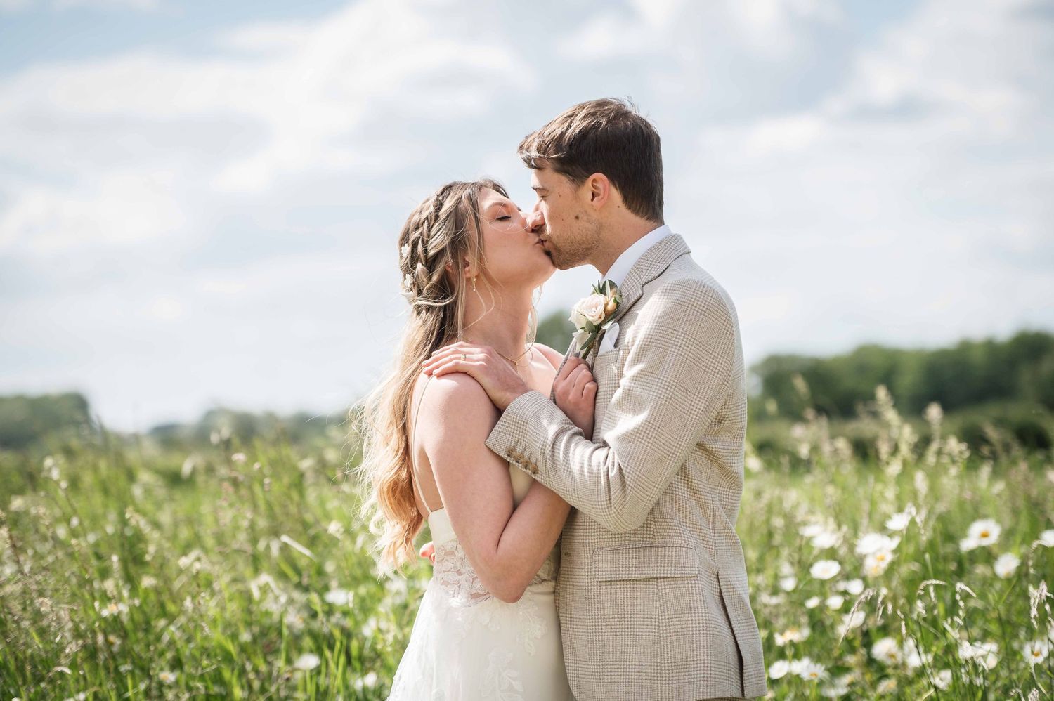 A romantic couple shares an intimate moment while standing in a sunlit meadow of white wildflowers.