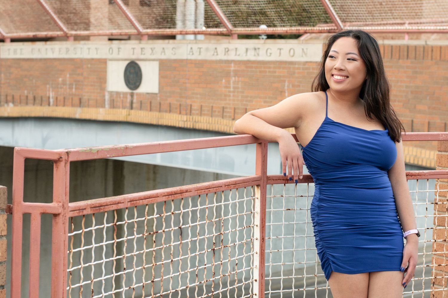 Woman in blue dress smiling while leaning on railing outdoors.