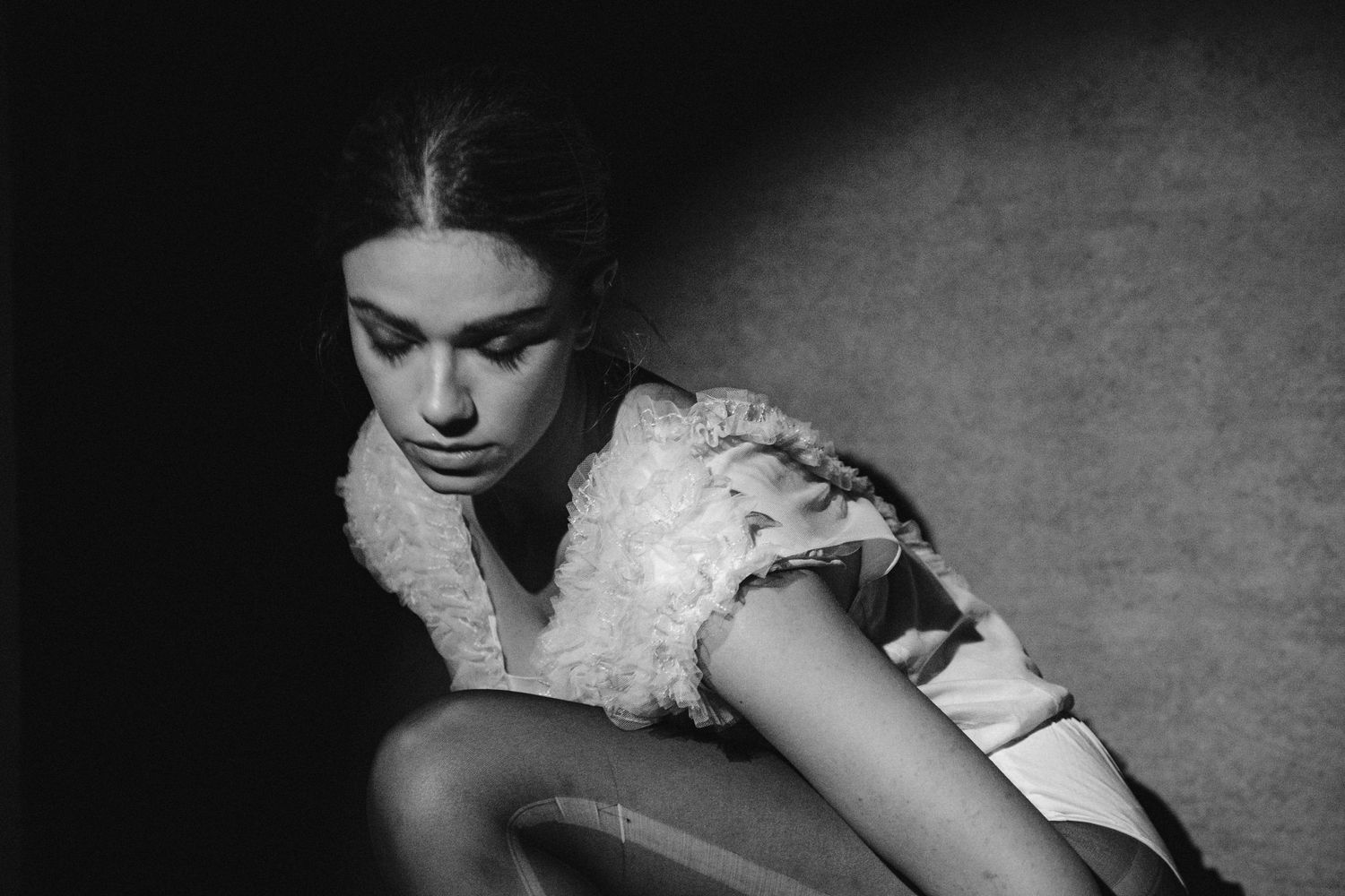 Artistic black and white photo of figure in lace dress crouching in dramatic lighting.