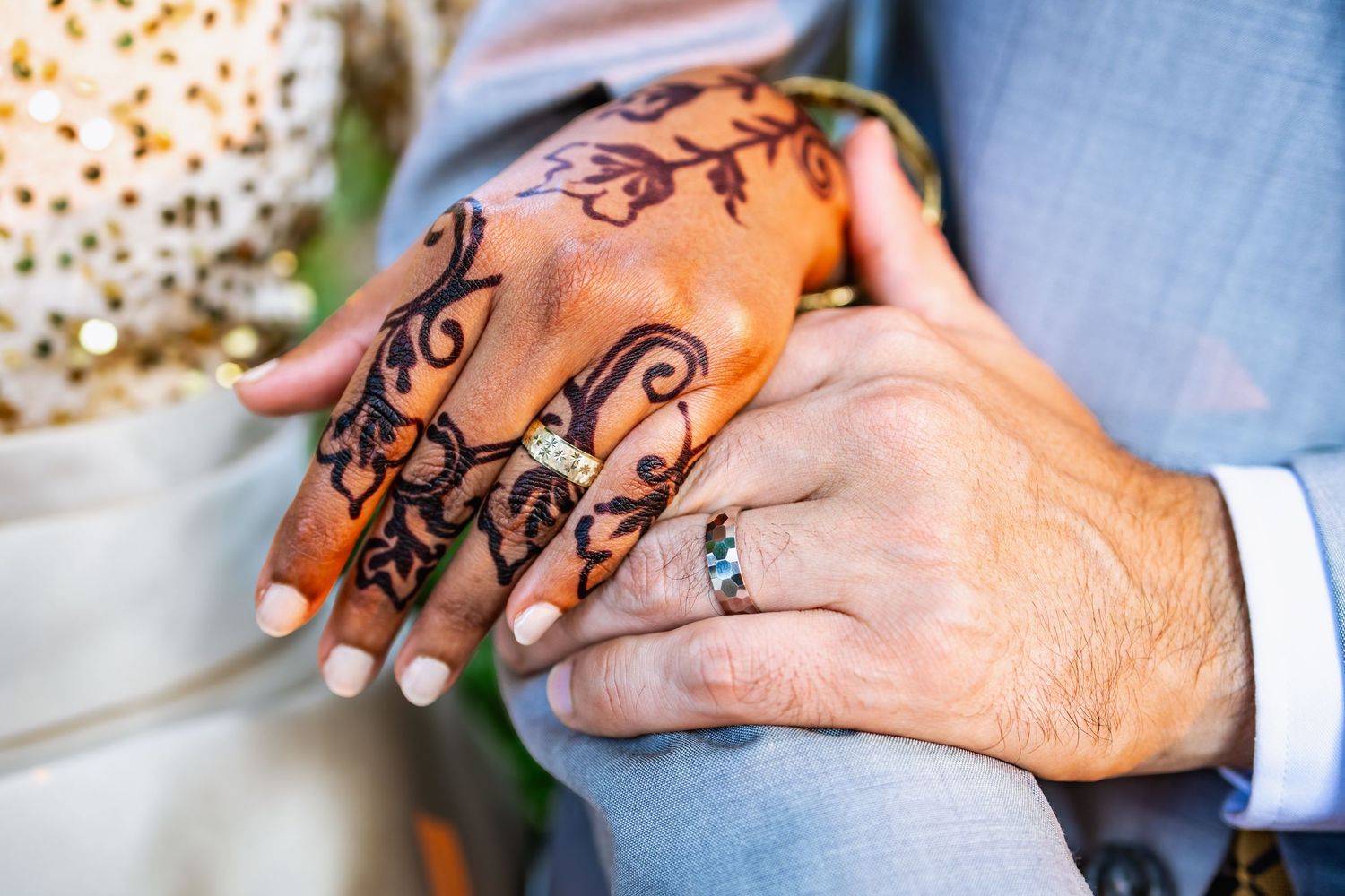 Close-up view of hands wearing wedding rings, with intricate henna design decorating one hand at traditional ceremony.